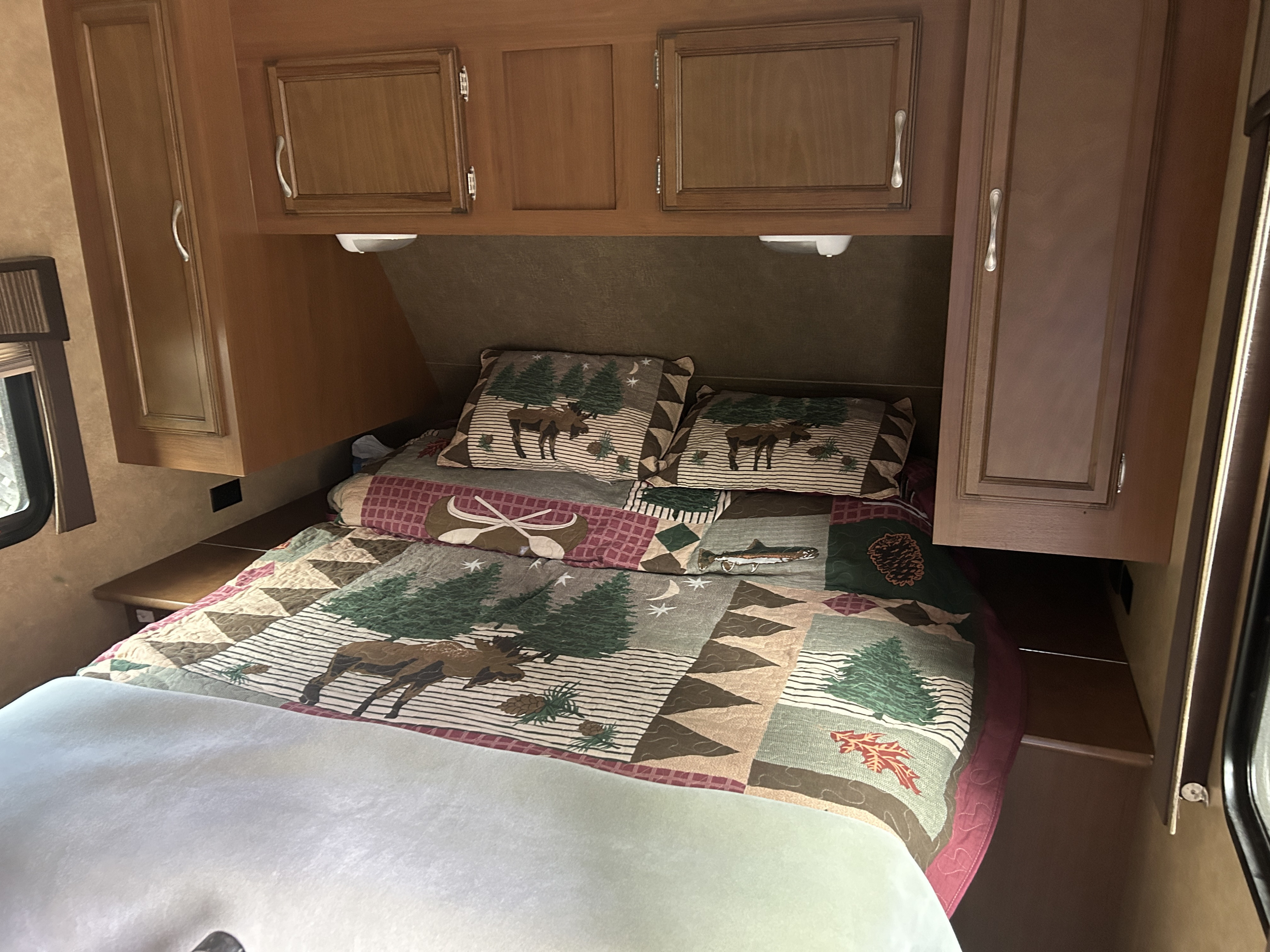 RV rental bedroom with a rustic, wildlife-themed quilt, matching pillows, overhead wooden cabinets, and convenient side shelves.. Starcraft Autumn Ridge 2014