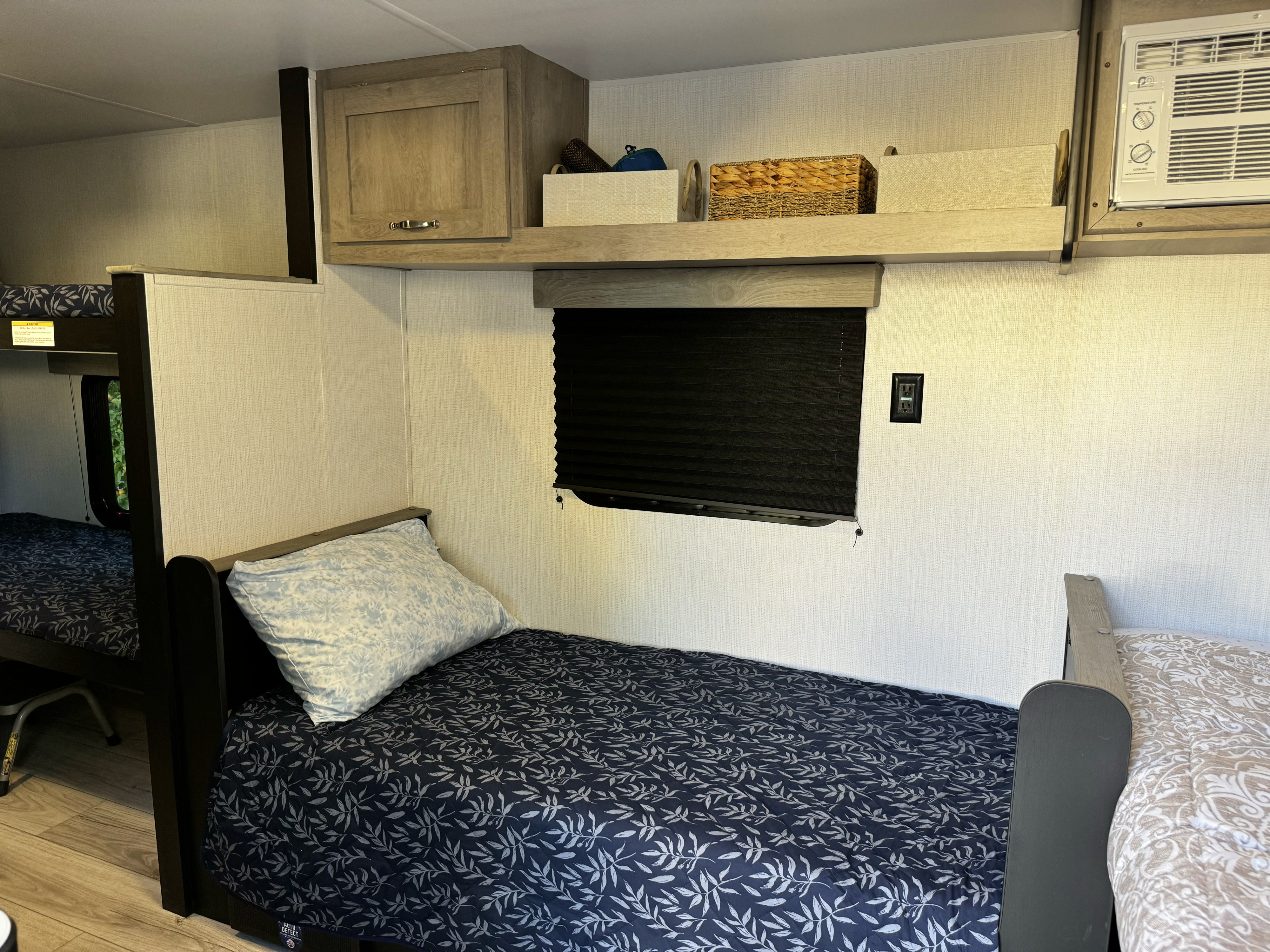 Inside an RV rental: cozy bunk beds with bedding, overhead storage, window with blinds, and AC unit for comfort.. Cruiser RV Avenir 2024