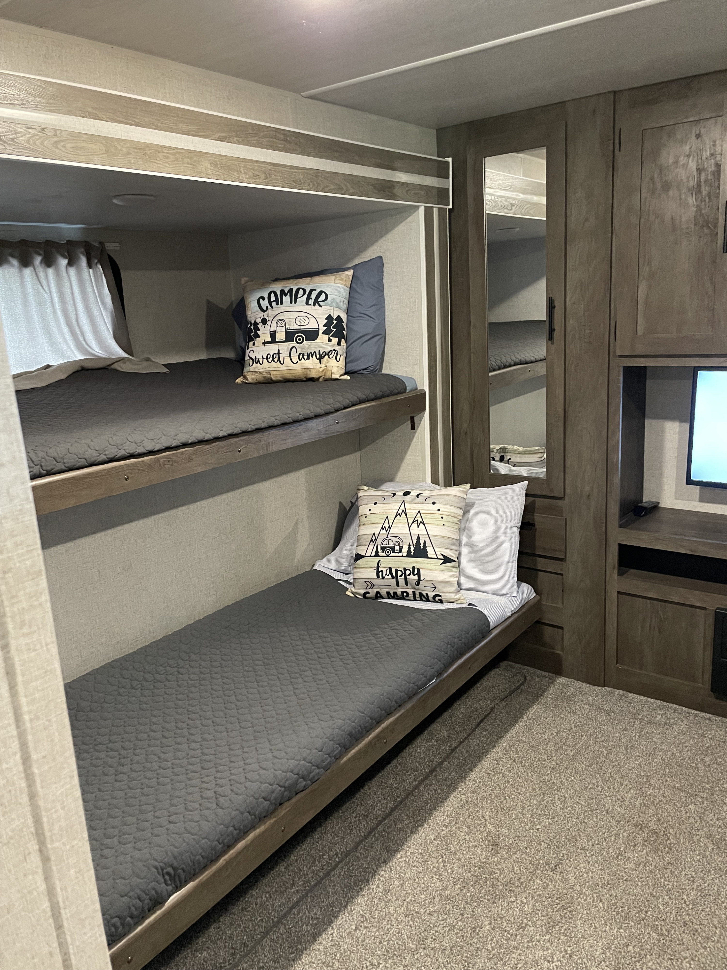 Inside an RV rental: cozy bunk beds with themed pillows. This comfortable camping space includes a TV, perfect for family adventures.. Forest River Wildwood 2021