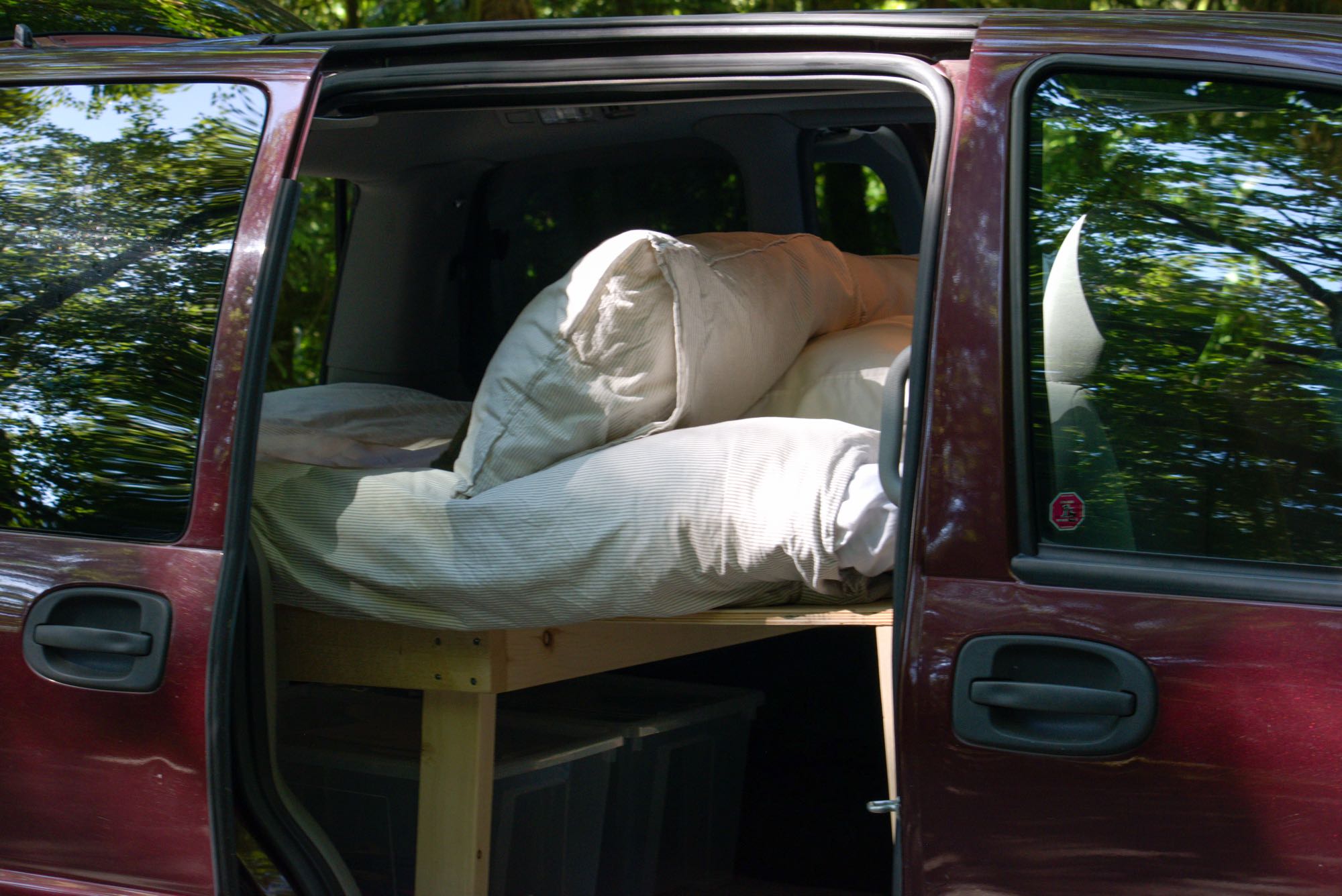 RV rental: Minivan's open door shows a bed built on a wooden frame with storage bins below.. Chevrolet Uplander 2008