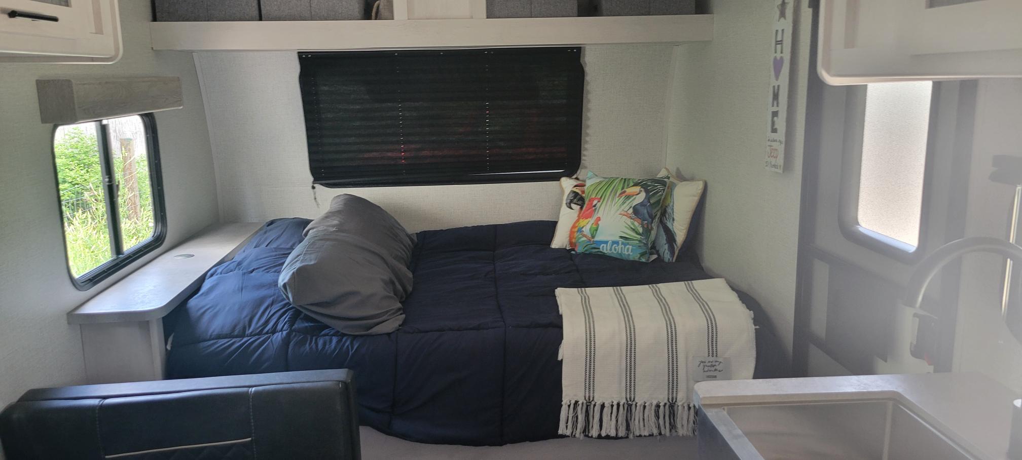 Cozy RV rental bedroom with tropical pillows & blackout blinds. Features a handy shelf & compact kitchen sink.. Dutchmen Coleman Rubicon 2021