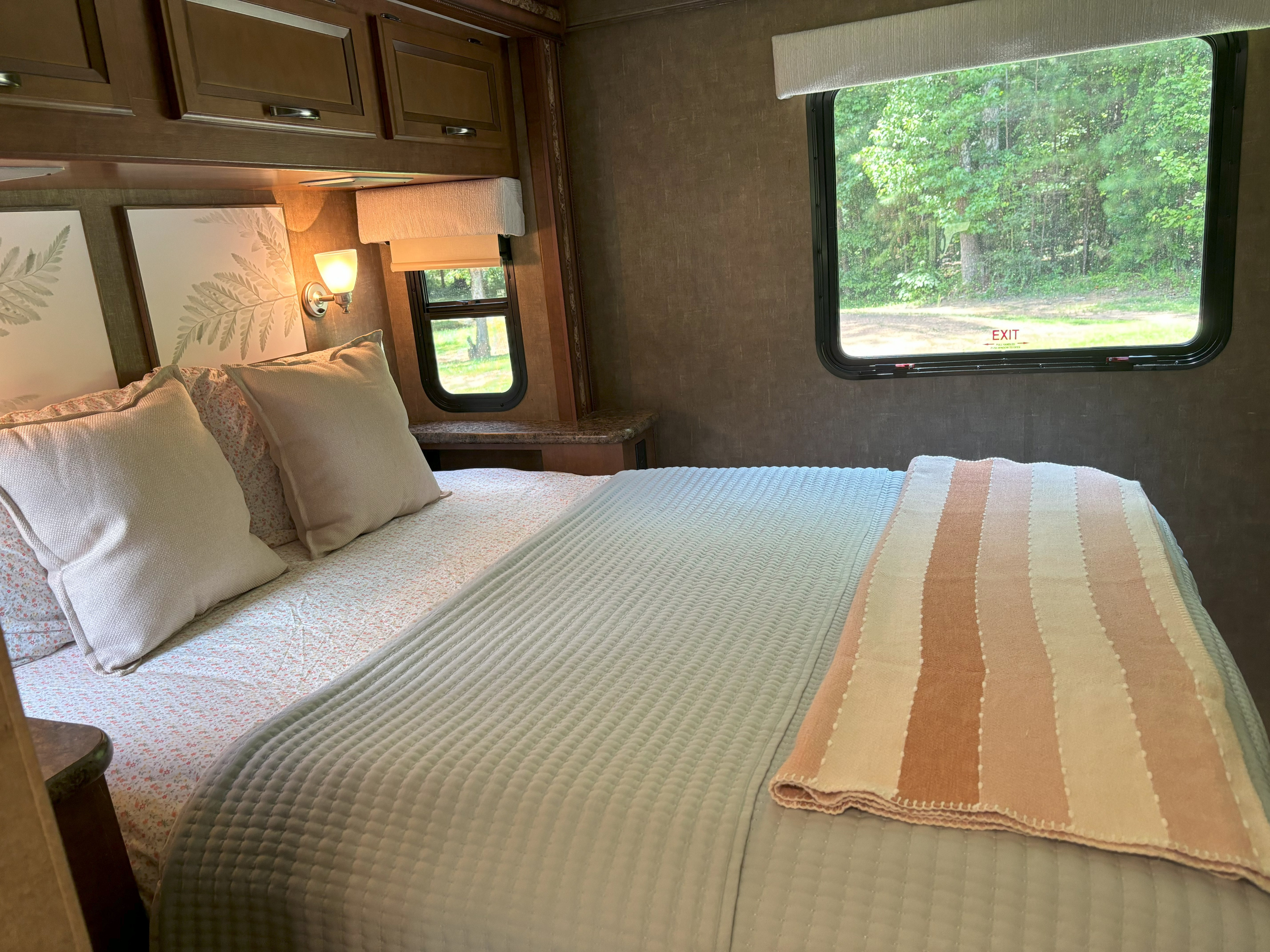 Cozy RV rental bedroom featuring a comfy bed with light bedding, a striped throw, and a window view of nature.. Thor Four Winds 2014