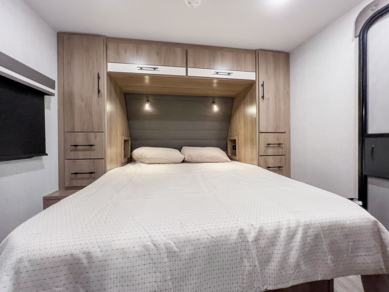 Cozy RV rental bedroom: a light bed with white comforter, flanked by wood-grain cabinets & reading lights.. Grand Design Imagine XLS 2023