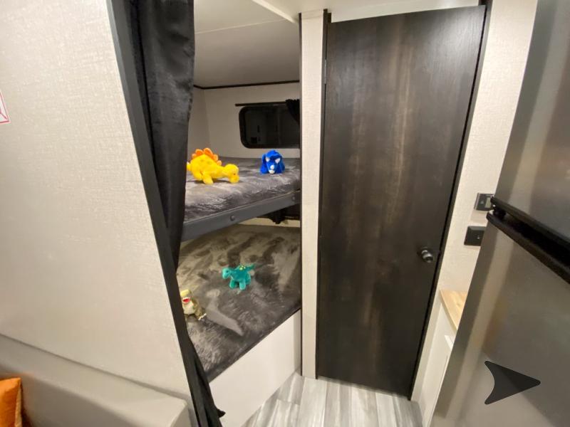 RV rental interior: cozy bunk beds with toys, privacy curtain, and dark wood door next to a fridge.. GOPLAY 26BH 2024