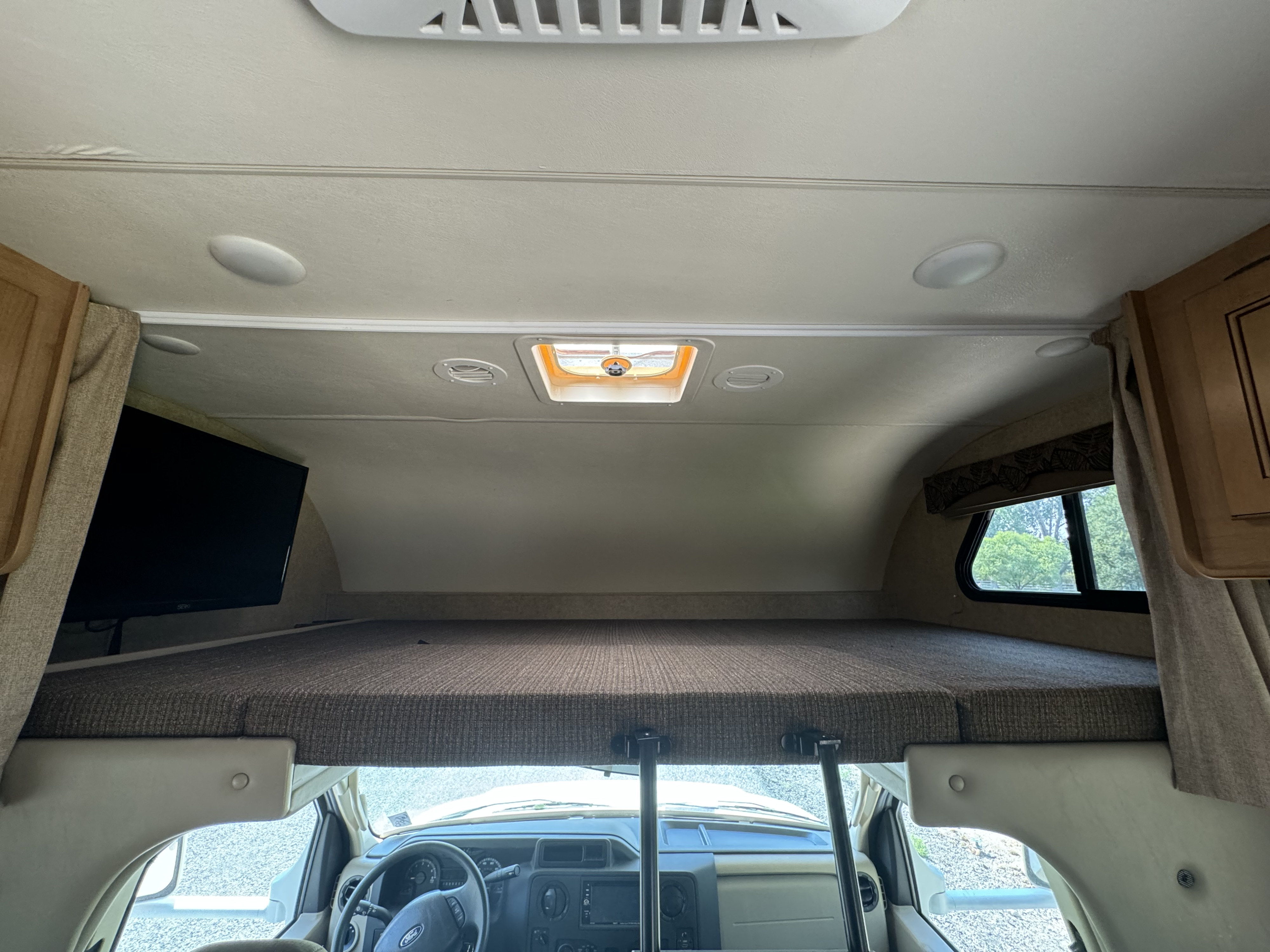 RV rental interior: comfy cab-over bunk bed, front dashboard, and TV, providing a cozy mobile home.. Thor Freedom Elite 2016