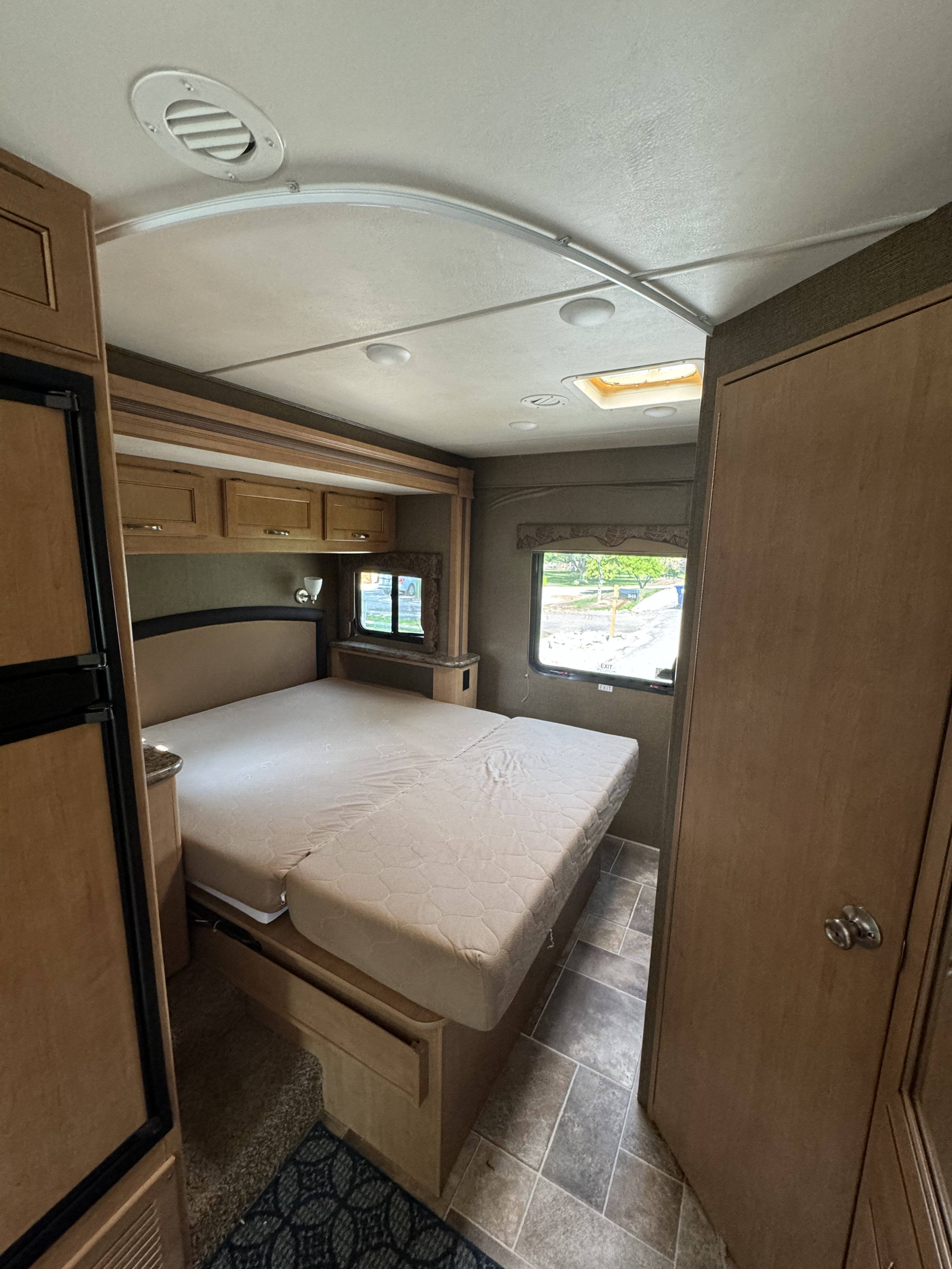 RV rental interior: A cozy bedroom with a large bed, wood cabinets, ceiling vent, and two windows for views.. Thor Freedom Elite 2016