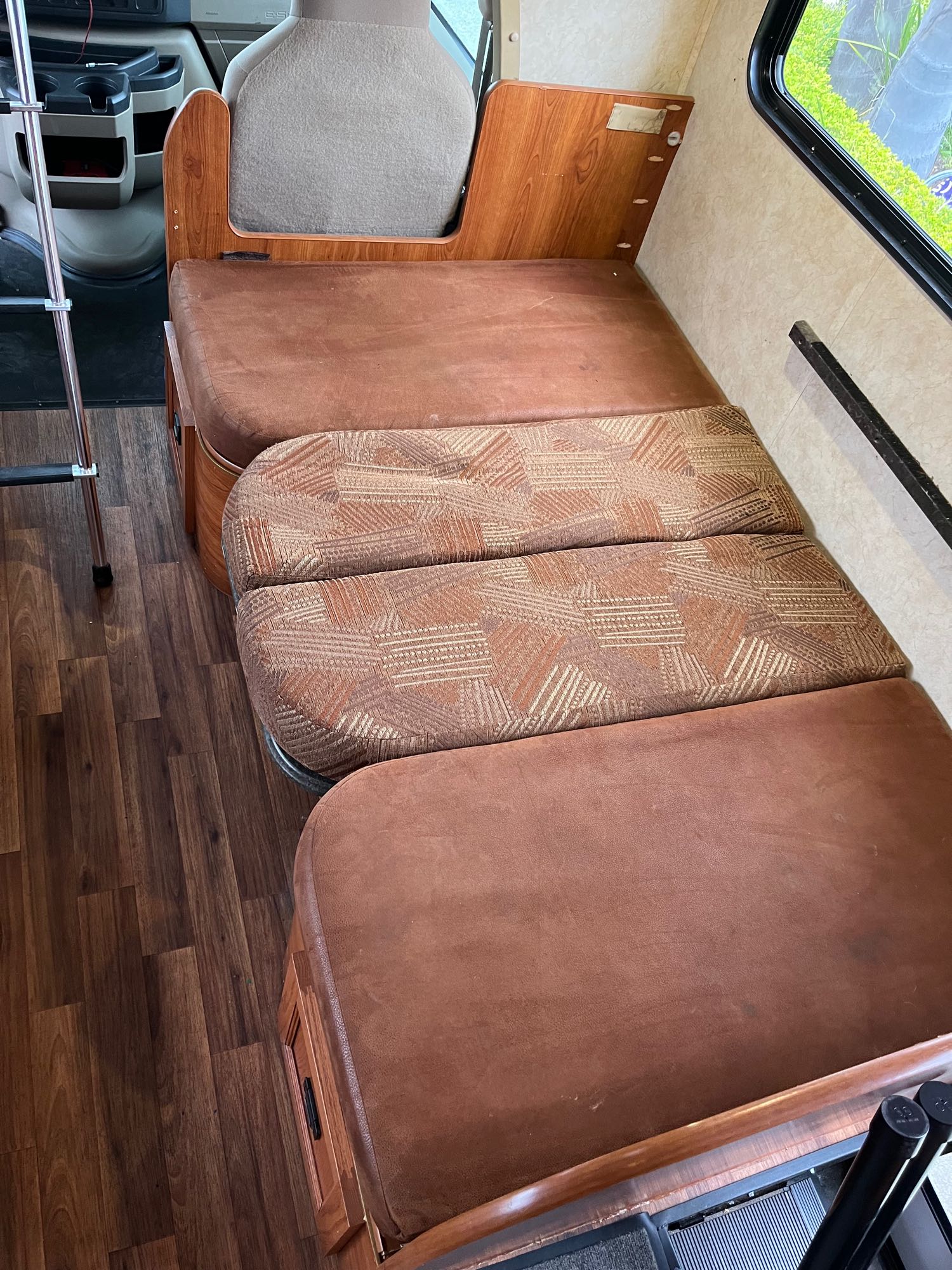 RV rental interior showing a dinette with brown and patterned cushions, wood floor, and bunk access ladder.. Coachmen Freelander 2011