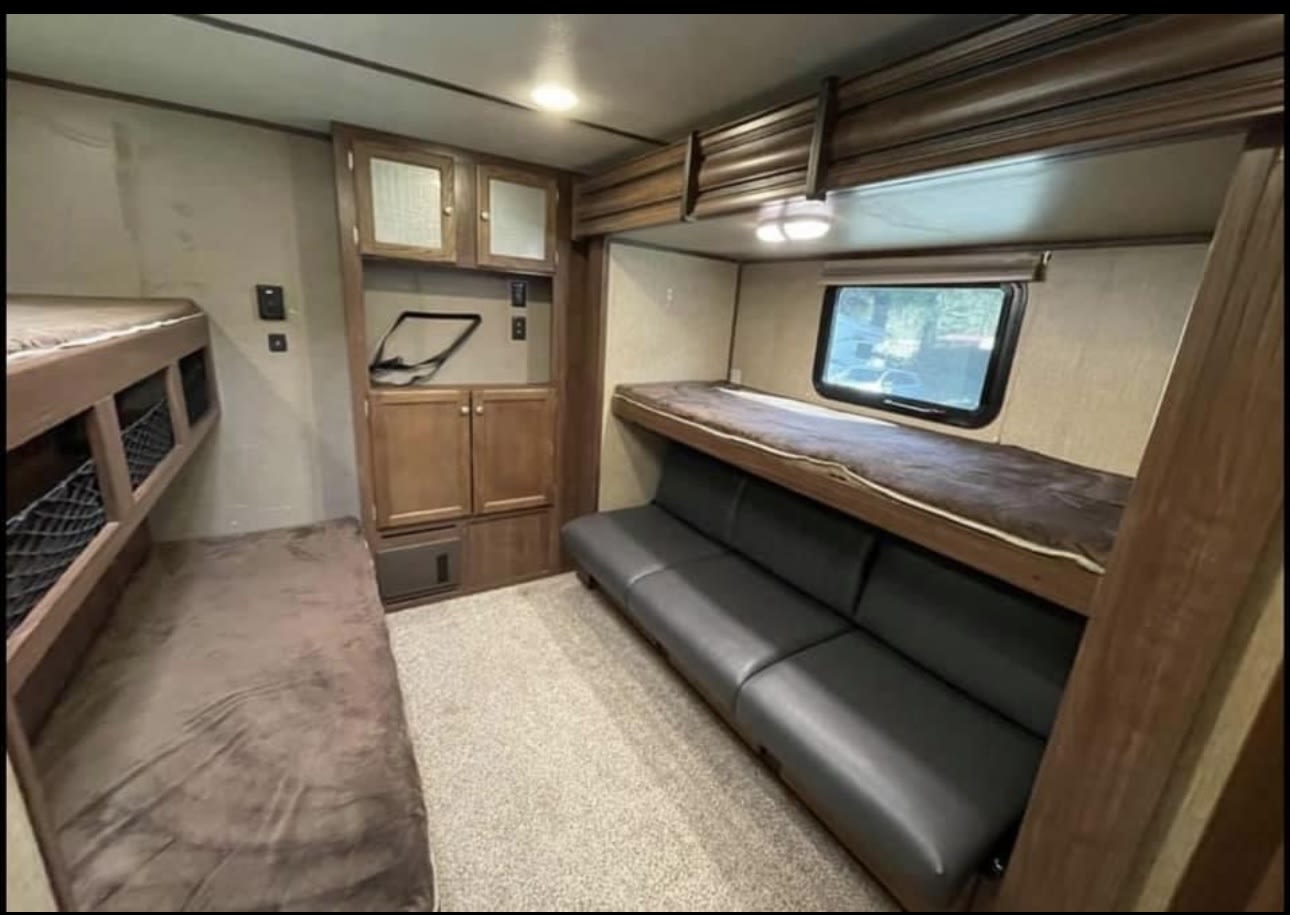 Inside an rv rental: bunk beds line the left, a black sofa and upper bunk on the right, with wood cabinets.. Keystone RV Sprinter Limited 2017