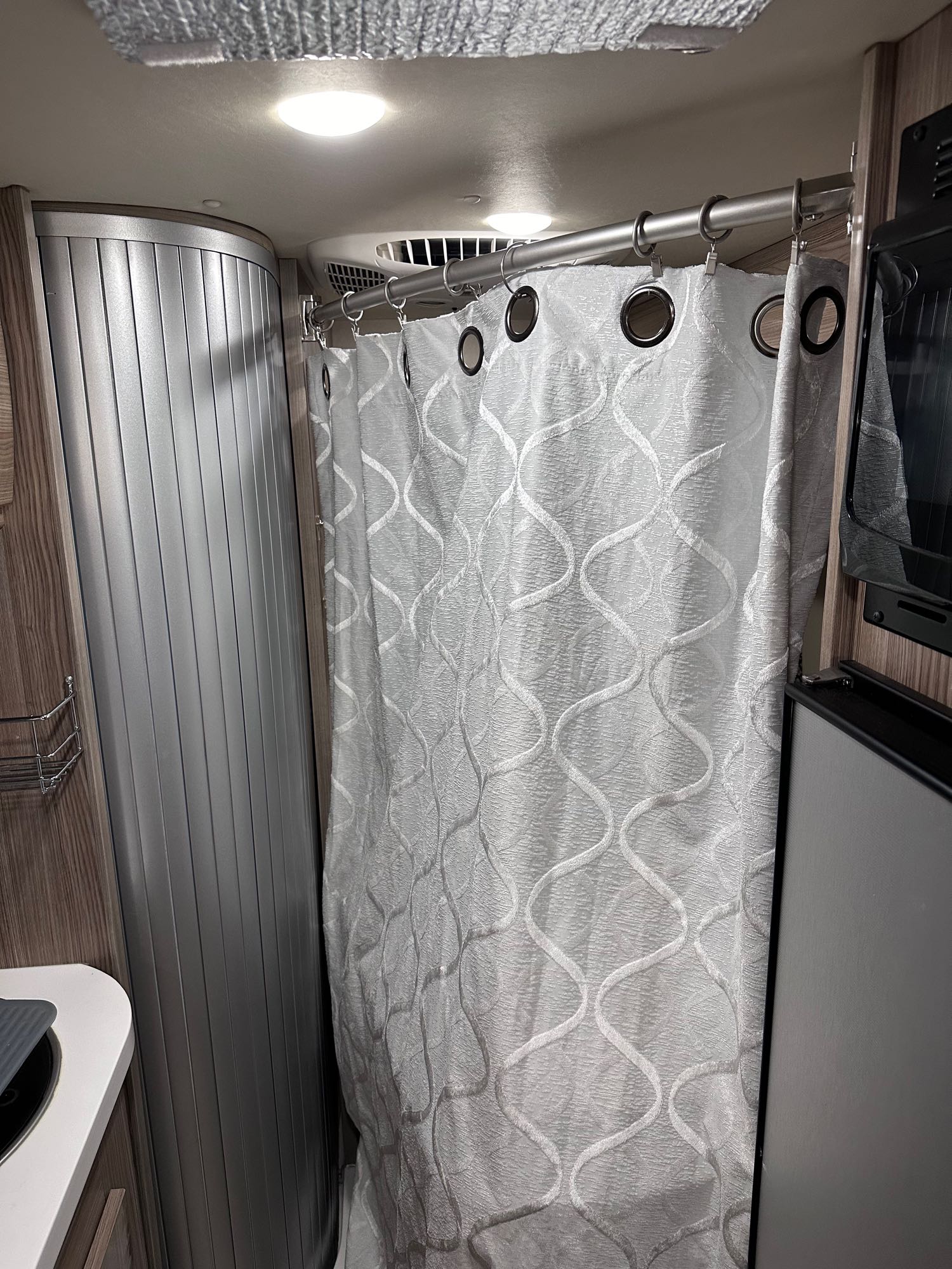 RV rental shower area: A patterned curtain, roll-up door, and nearby fridge showcase compact, functional RV interior amenities.. Winnebago Travato 2022