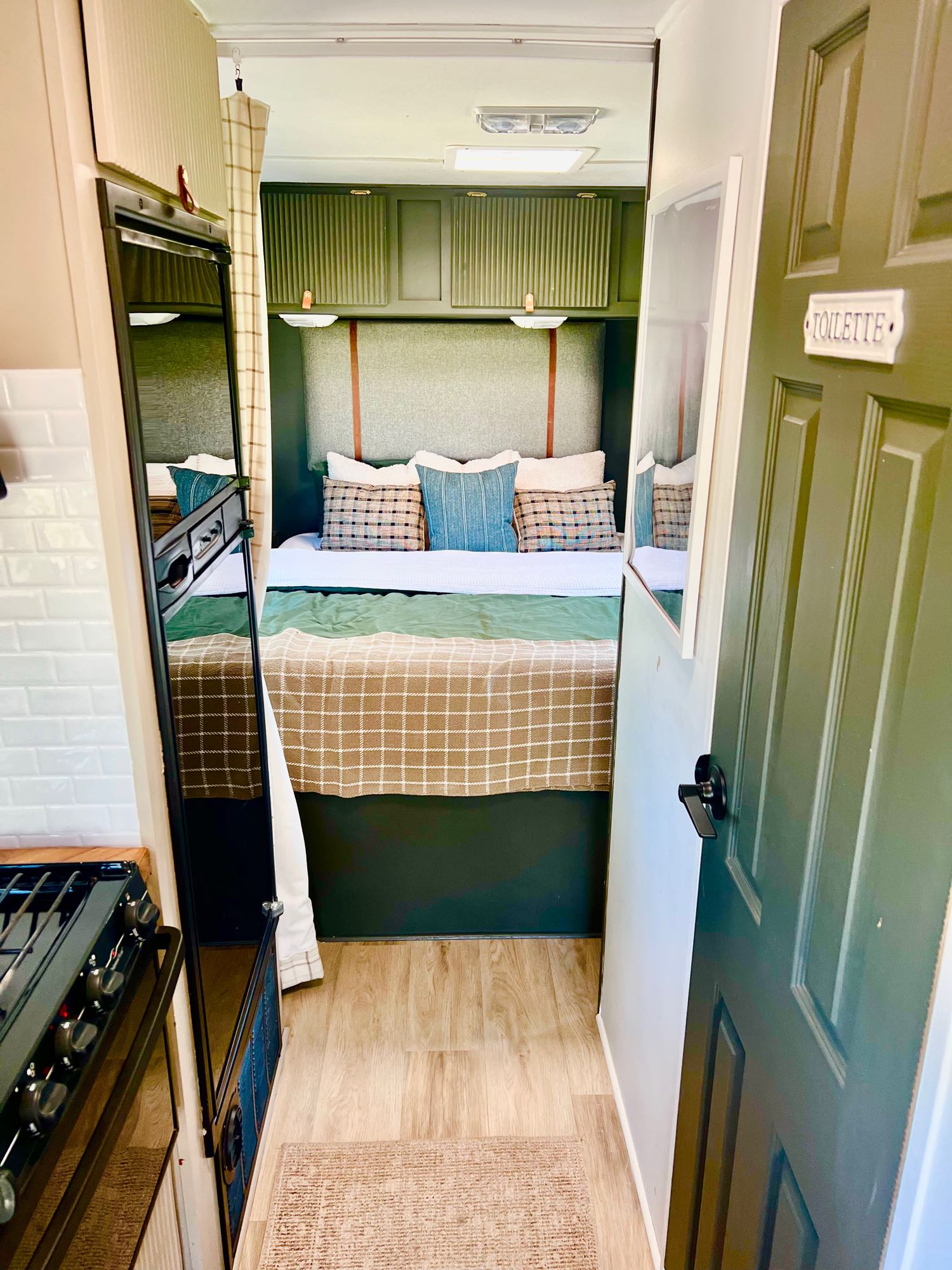 Modern RV rental interior showcasing a cozy bedroom with green and plaid bedding, a compact kitchen, and a "TOILETTE" door.. Ford Atlantis Ford Transit 2008