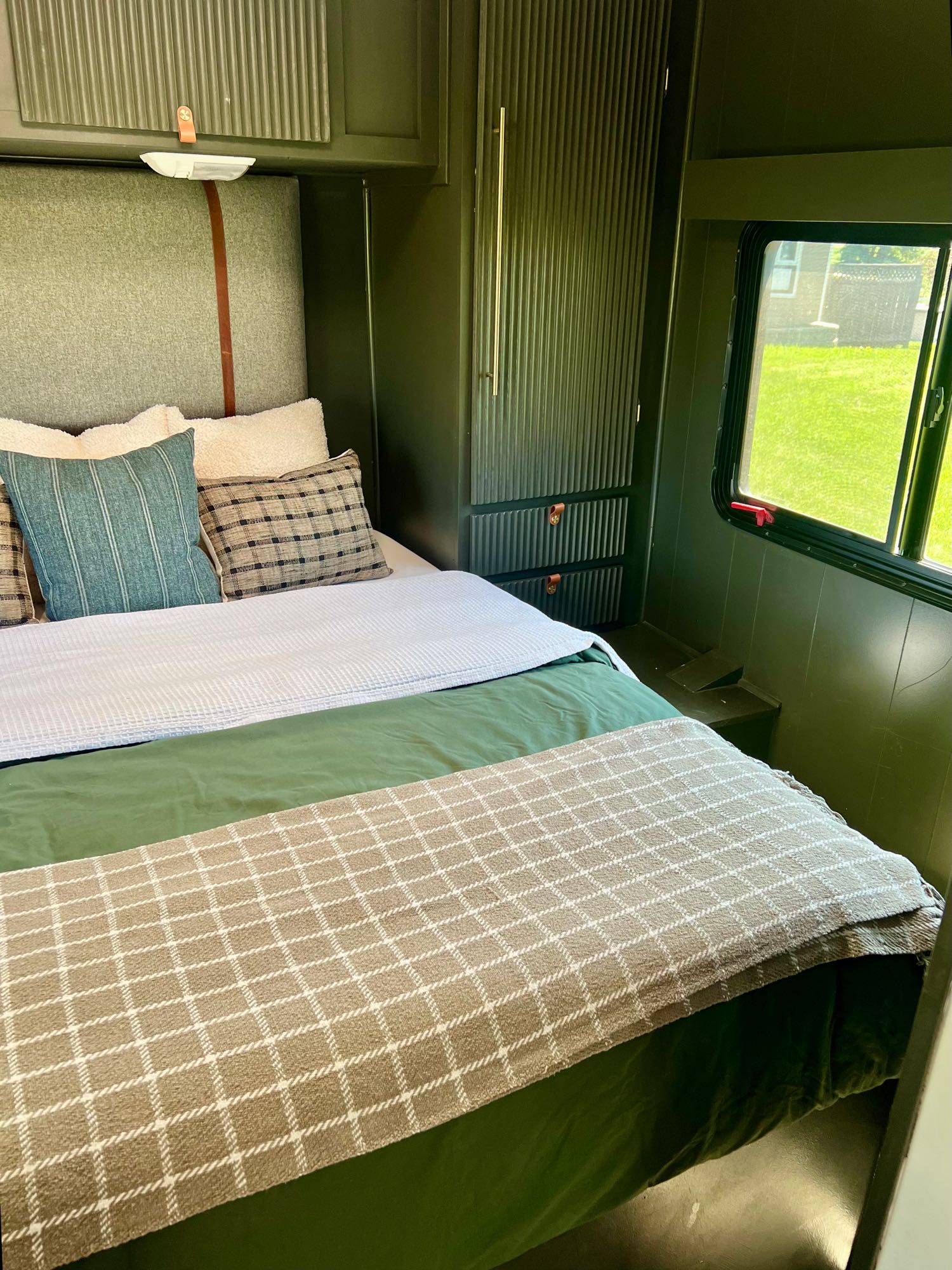 Explore this cozy RV rental bedroom. It boasts modern dark green interiors, comfortable layered bedding, and practical built-in storage.. Ford Atlantis Ford Transit 2008