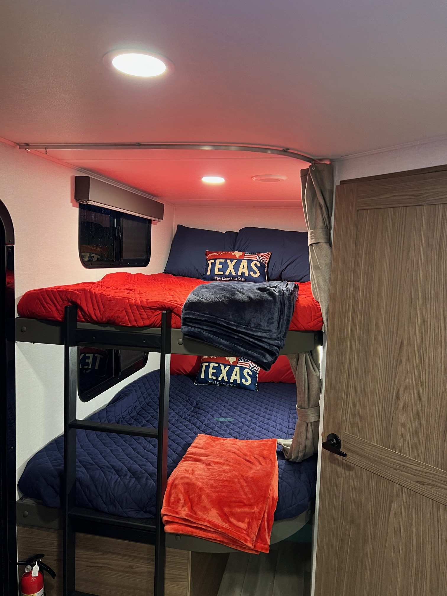 Cozy RV rental interior showcasing red and blue bunk beds with Texas-themed pillows under warm ambient lighting.. Alliance Delta 251BH 2024