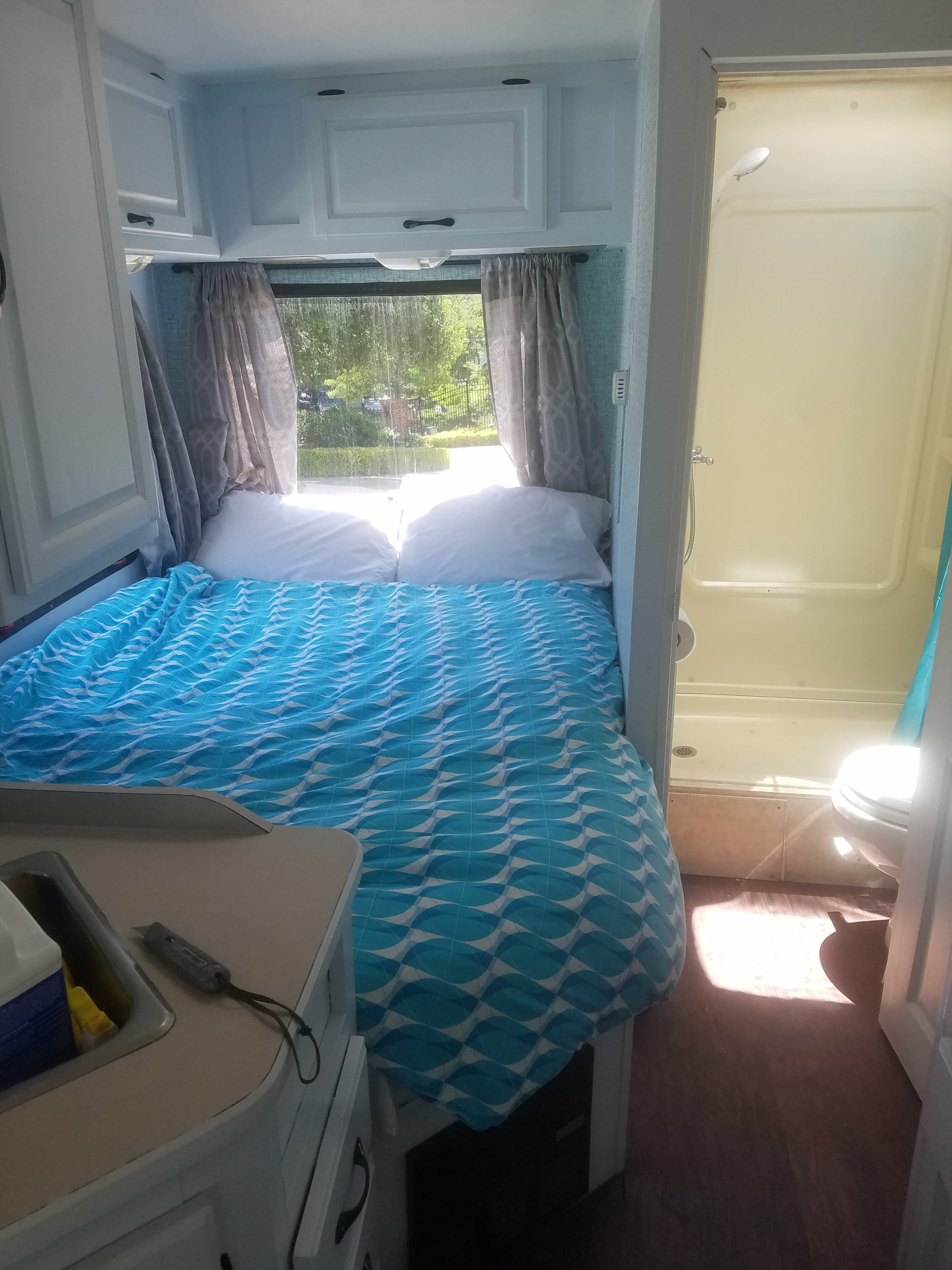 Inside a bright rv rental: a cozy bed with blue bedding, overhead cabinets, a sink, and a compact bathroom with shower and toilet.. four winds majestic 2004