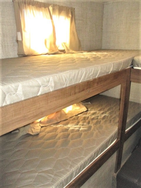 Interior view of an RV rental showing stacked bunk beds with mattresses and a brightly lit window.. Gulf Stream Kingsport 2020