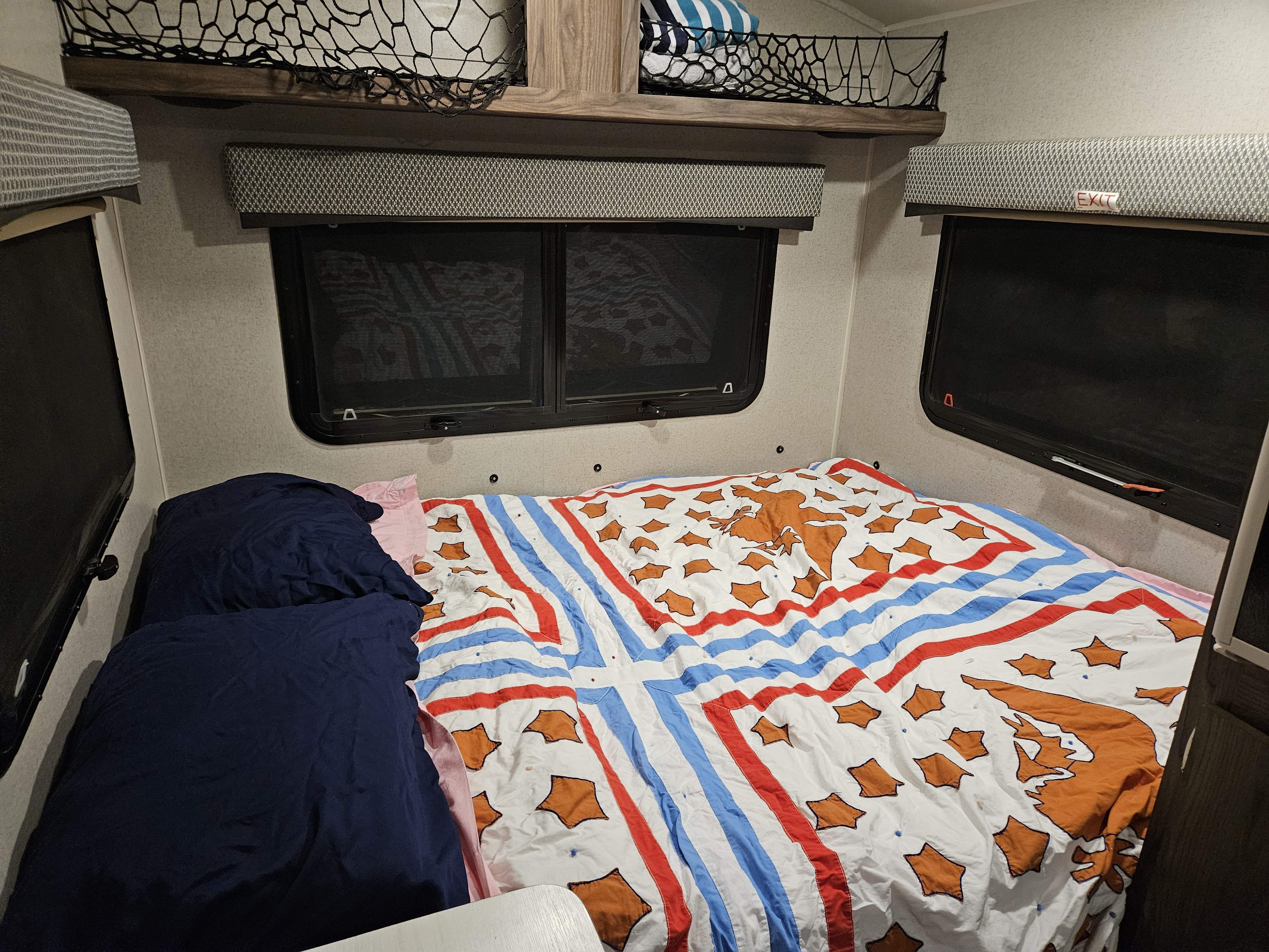 RV rental bedroom: Cozy interior with bed, colorful bedding, side windows, overhead storage, and an EXIT sign.. Forest River Rockwood Geo Pro 2018