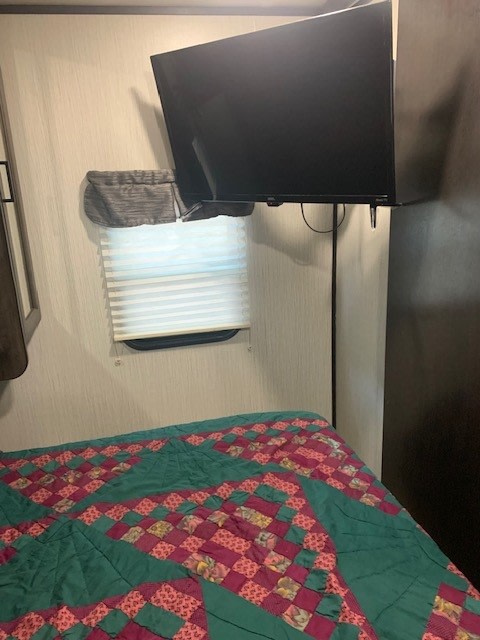 Cozy RV rental bedroom with a quilted bed, window blinds, and wall-mounted TV, ideal for travel.. Heartland RVs Mallard 2021