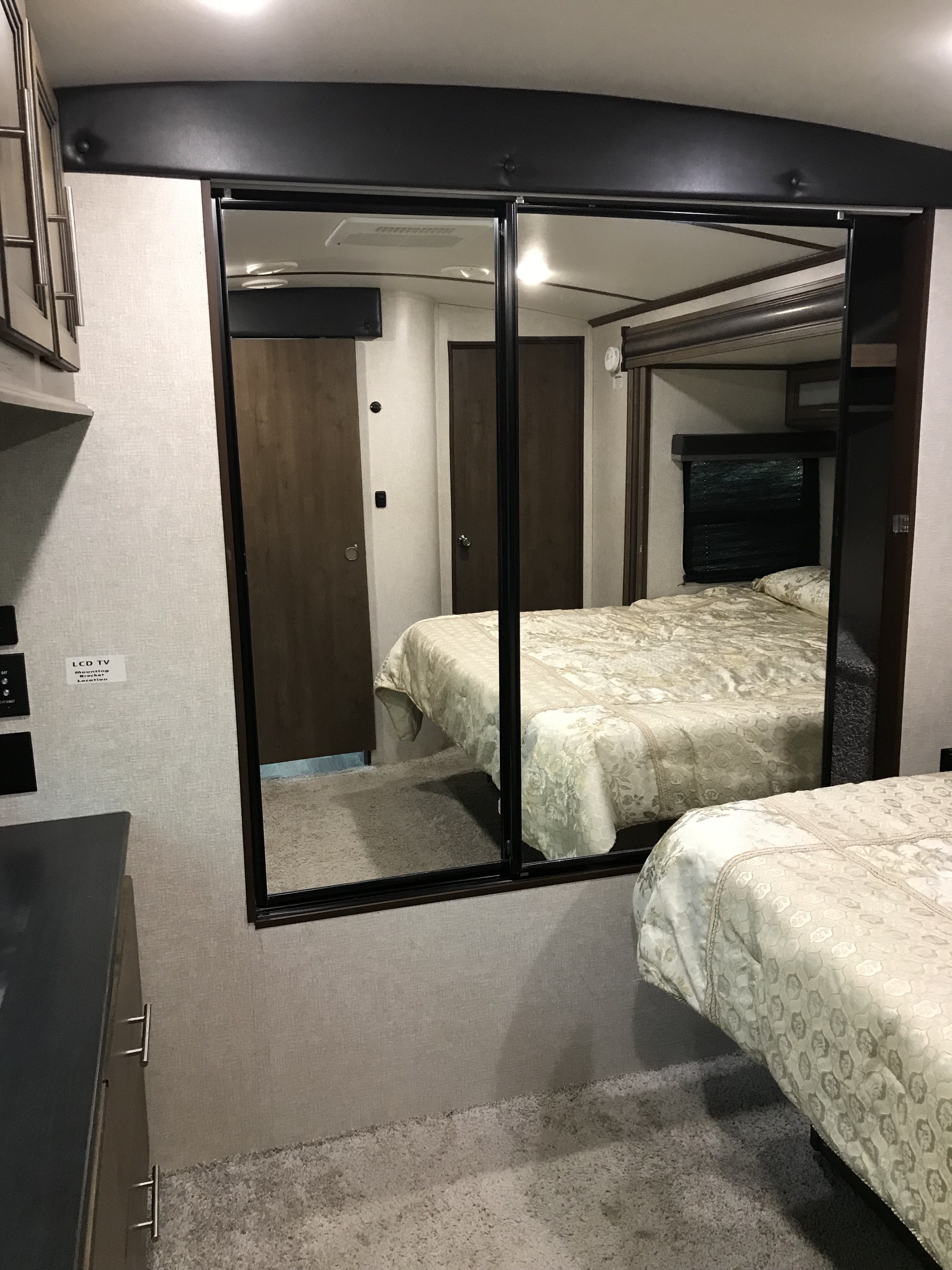 Inside an RV rental bedroom: dual mirrored closet doors reflect a cozy bed with a patterned comforter and soft carpet.. Keystone RV Cougar 2020