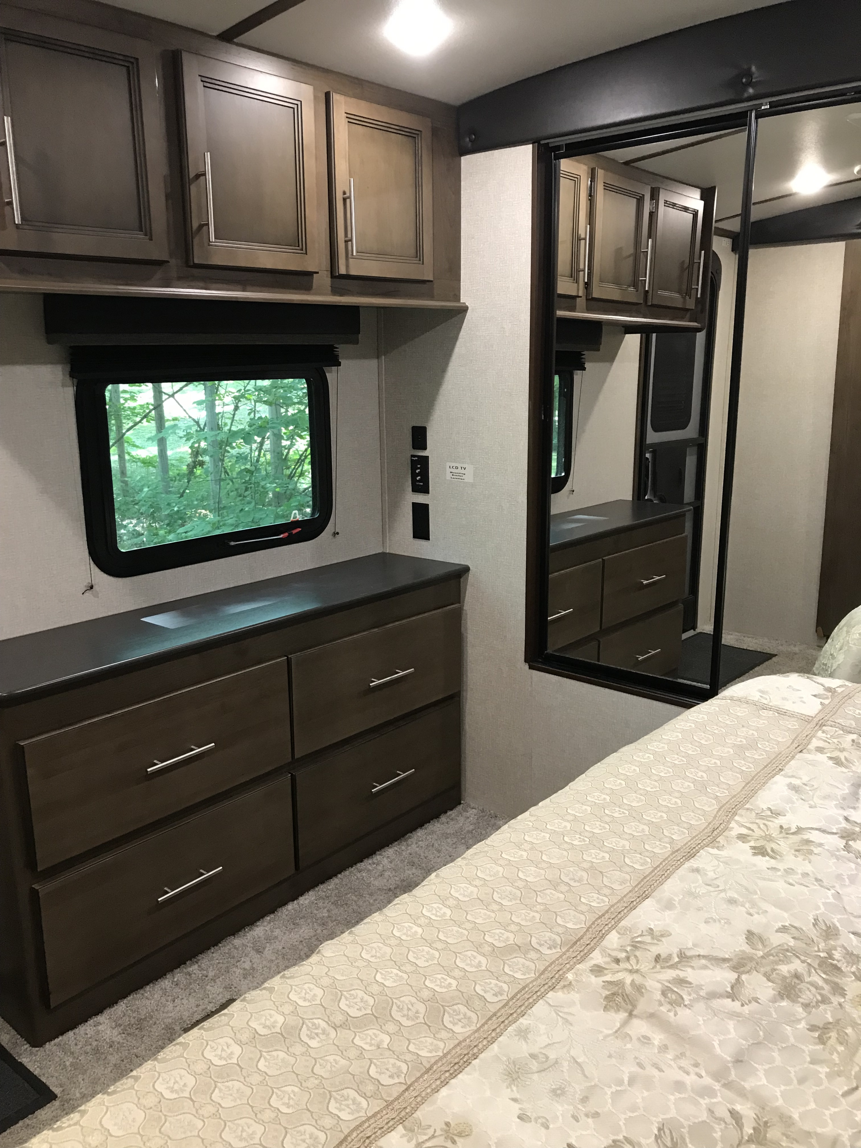 Comfortable RV rental bedroom featuring a dresser, mirrored closet, ample cabinets, and a window with a serene tree view.. Keystone RV Cougar 2020