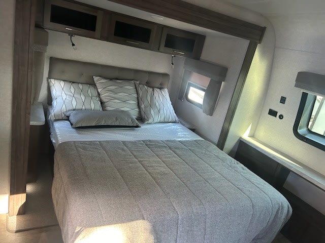 This RV rental bedroom features a comfortable bed with pillows, overhead cabinets, and windows for a cozy travel stay.. Flagstaff Super Lite 2022
