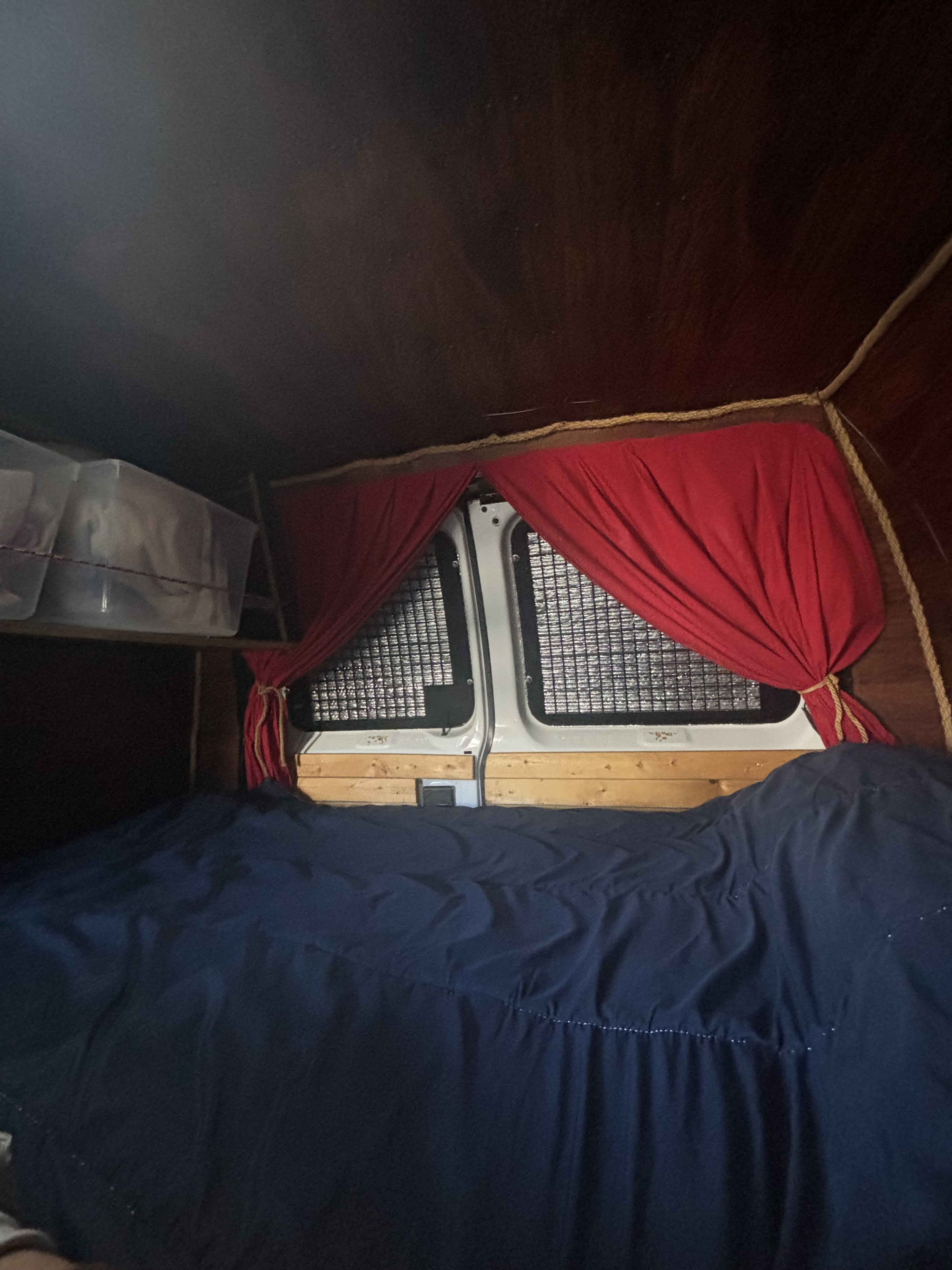 Dark, cozy RV rental interior showing a bed, overhead storage bins, and red privacy curtains on the rear doors.. Ford Ford E350 2009