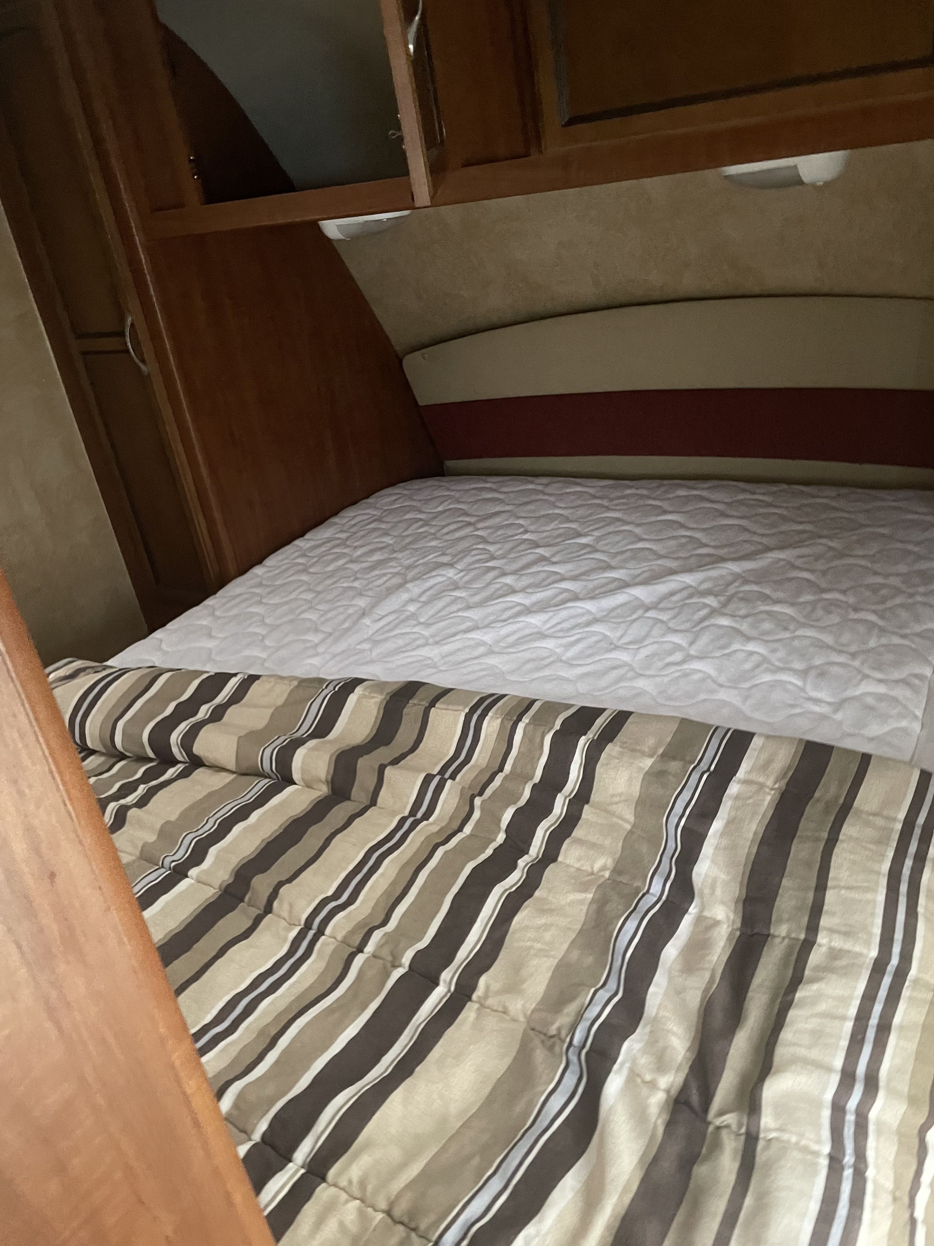 Inside an RV rental: a cozy bed with a striped comforter, white mattress pad, and built-in wooden storage.. Jayco Jay Feather 2011
