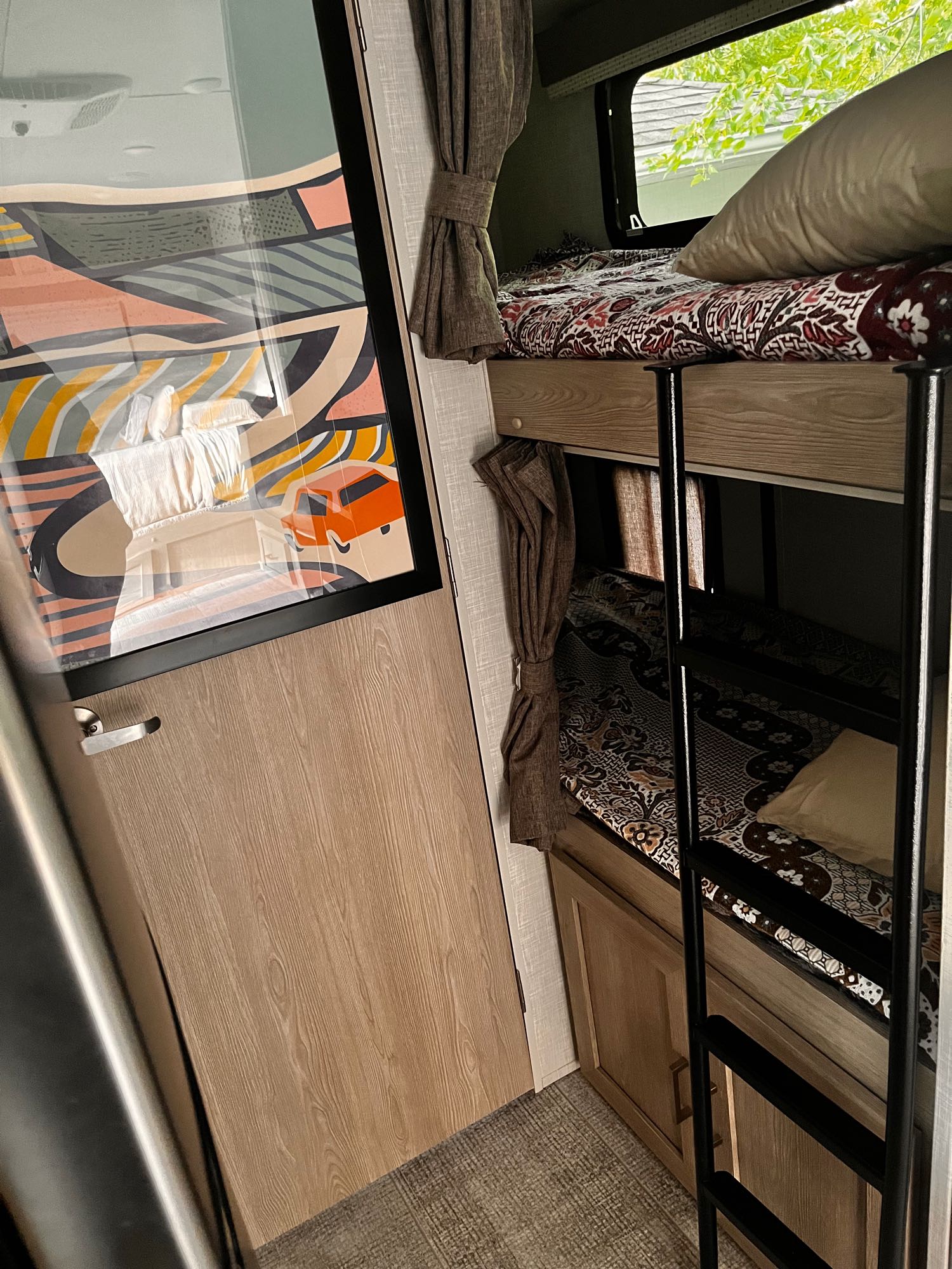 Inside an RV rental: cozy bunk beds with patterned blankets, a ladder, and a door with modern art. Ideal for family adventures.. Forest River Rockwood Geo Pro 2021