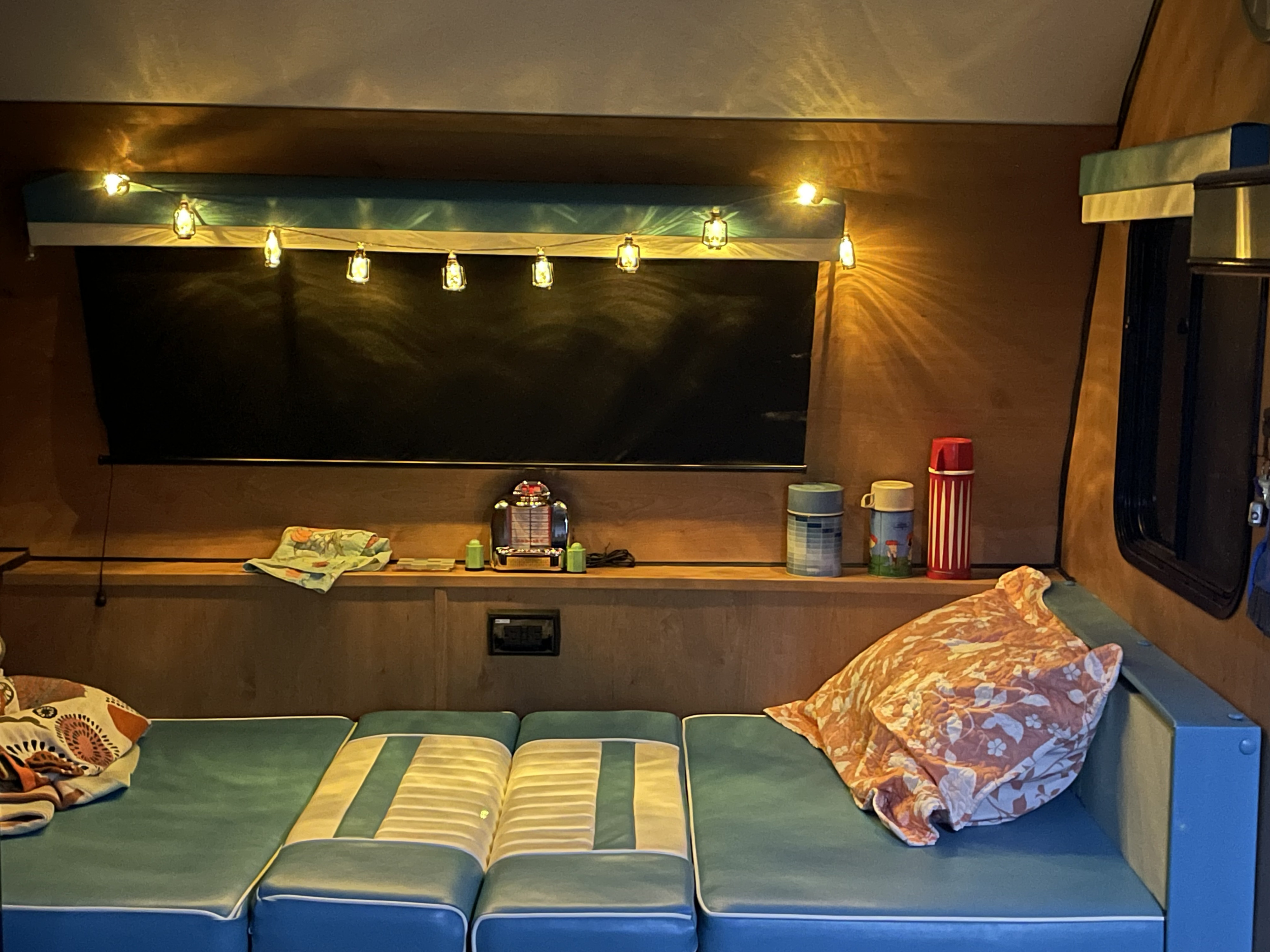 Relax and unwind in this cozy rv rental! Features warm string lights, a screen, and comfortable blue seating with patterned cushions.. Riverside Retro Elite 2024
