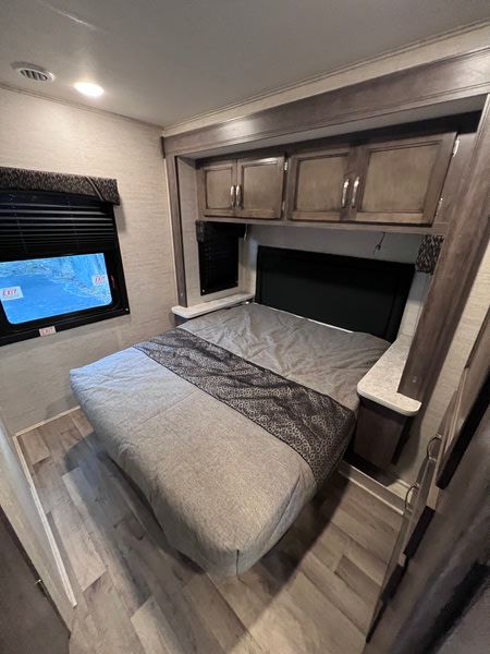 Comfortable RV rental bedroom featuring a bed, overhead cabinets, and a window for natural light.. Jayco Redhawk SE 2022