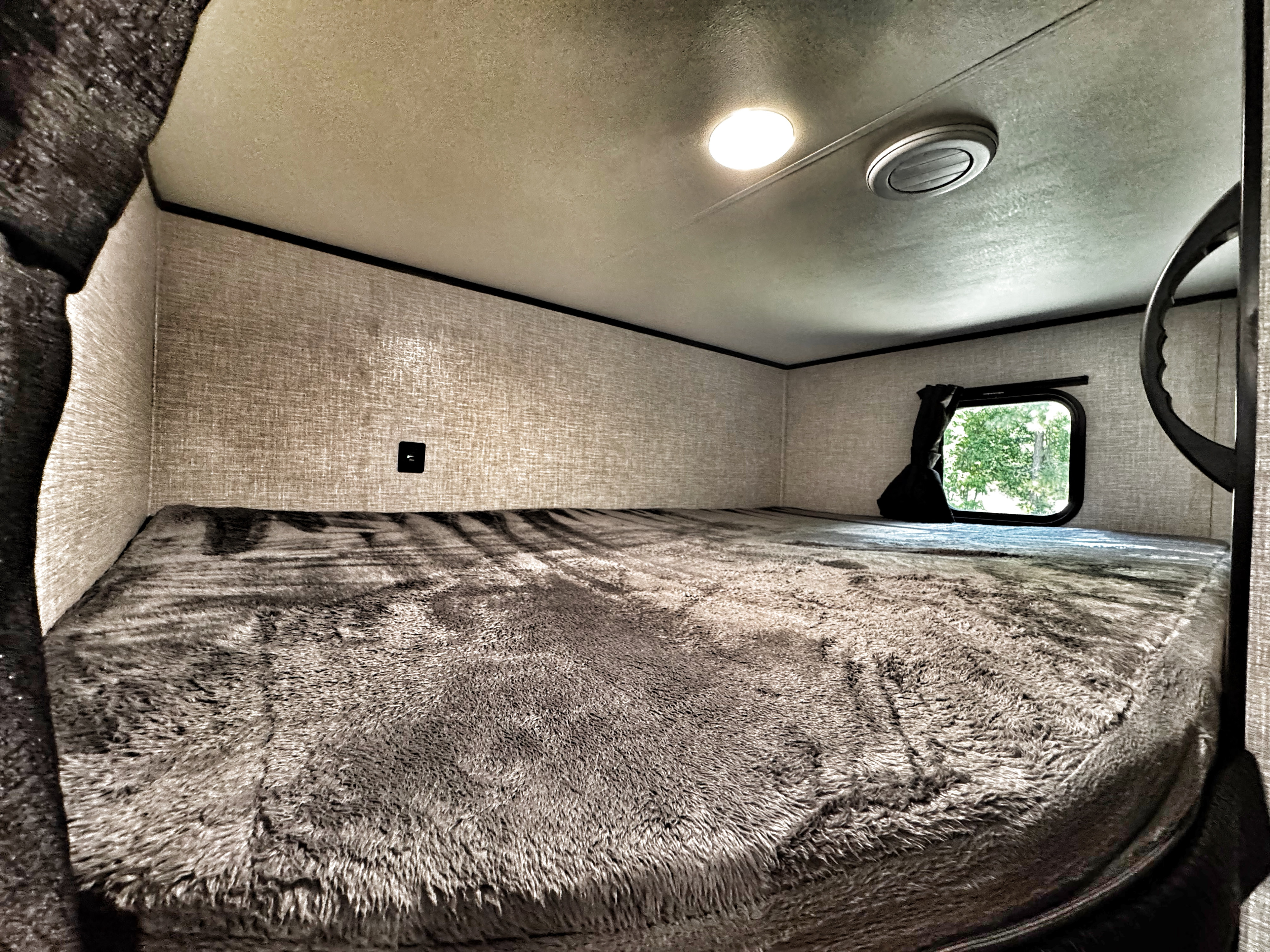 Inside an RV rental: a cozy bunk bed with gray blanket, window view, and charging port. Ideal for camper travel.. Jayco Jay Flight SLX 2022