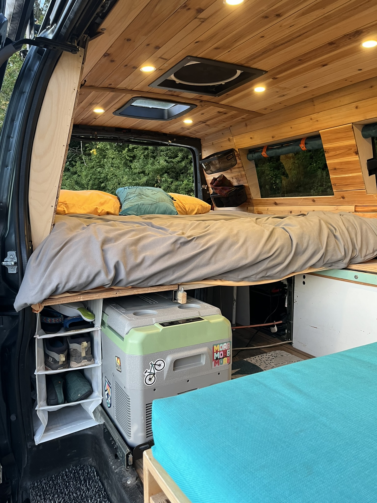 View of a modern RV rental interior featuring a cozy raised bed, wood-paneled ceiling, fridge, and built-in storage.. Gmc Savanna C1500 2014
