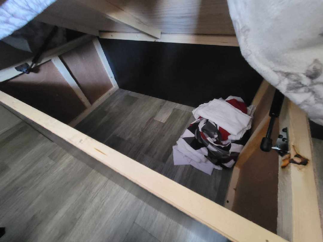 Open RV rental under-bed storage reveals wooden frame, black gas strut, and folded clothing. Practical travel space.. Jayco Jay Flight SLX 8 2022