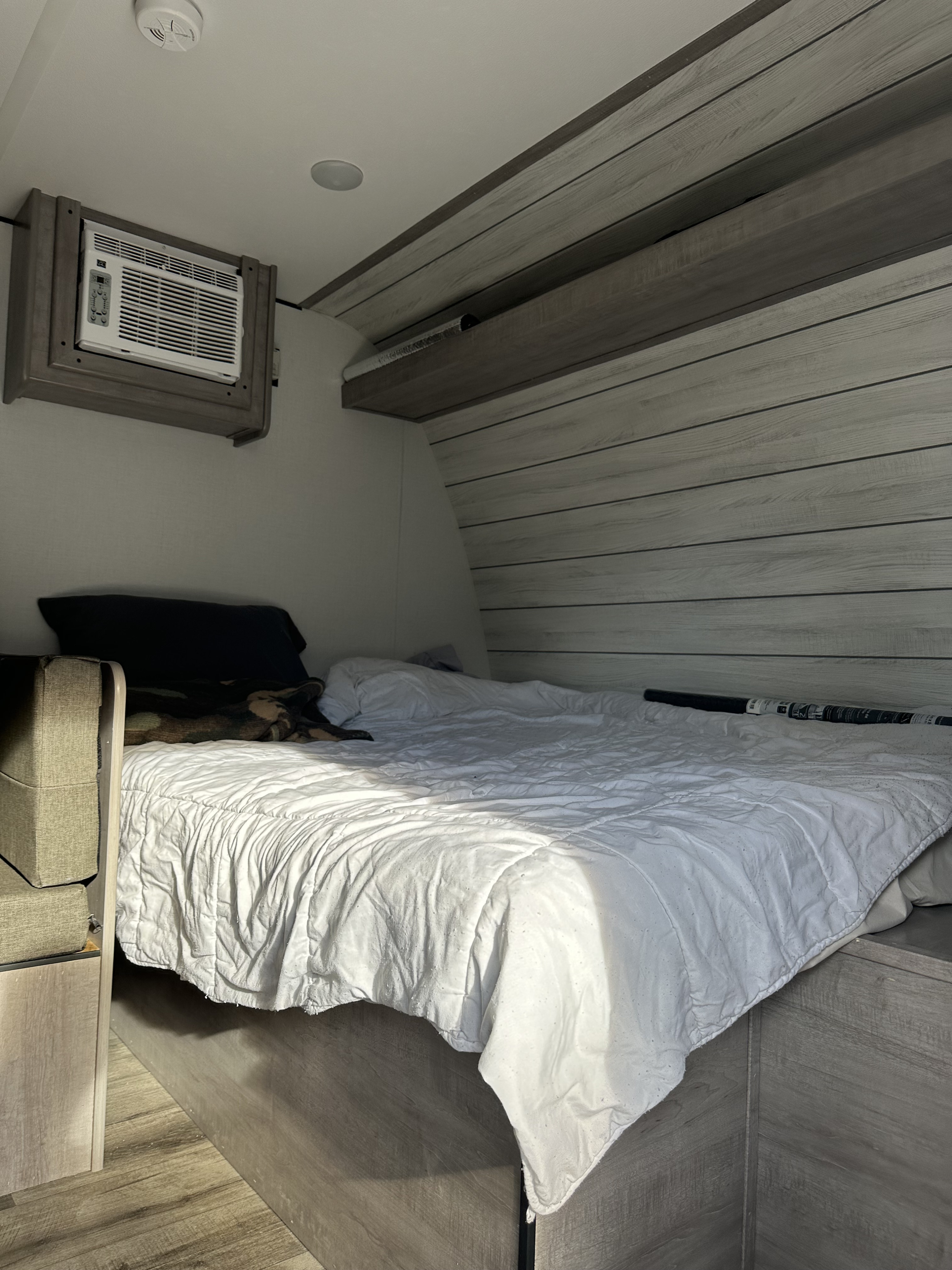 RV rental bedroom interior: a white-covered bed, wall-mounted AC, and wood paneling offer a comfortable stay.. Coleman Lantern 17B 2024