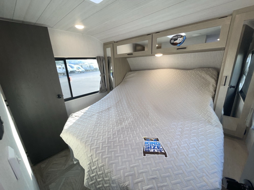 Spacious RV rental bedroom featuring a king-size bed (66"x78") with white bedding, overhead storage, and a window.. Forest River Salem Platinum 2024