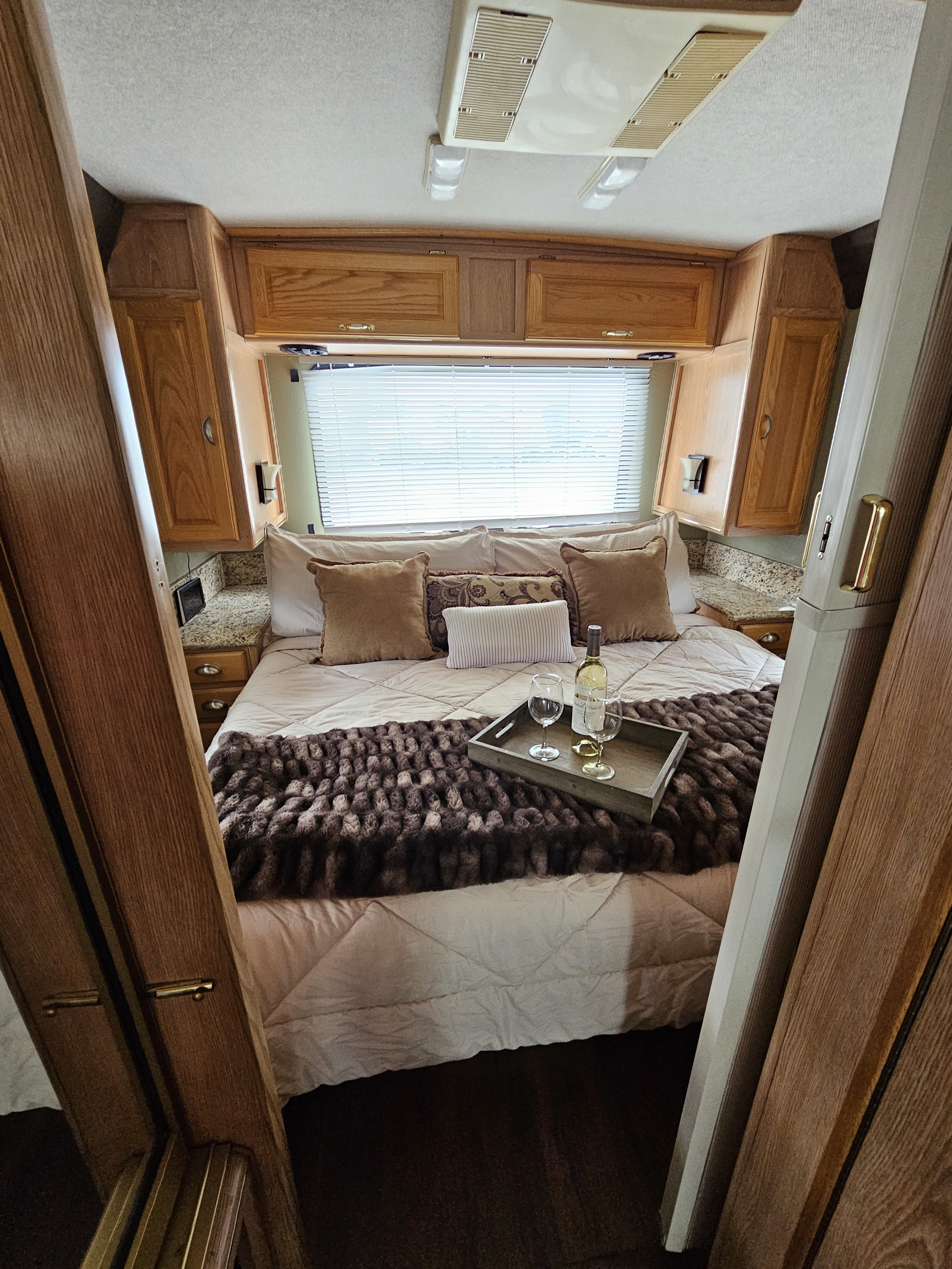 Inviting RV rental bedroom setup: a bed with plush blankets, wine tray, and classic wood interior.. Rexhall Xl3250 1995