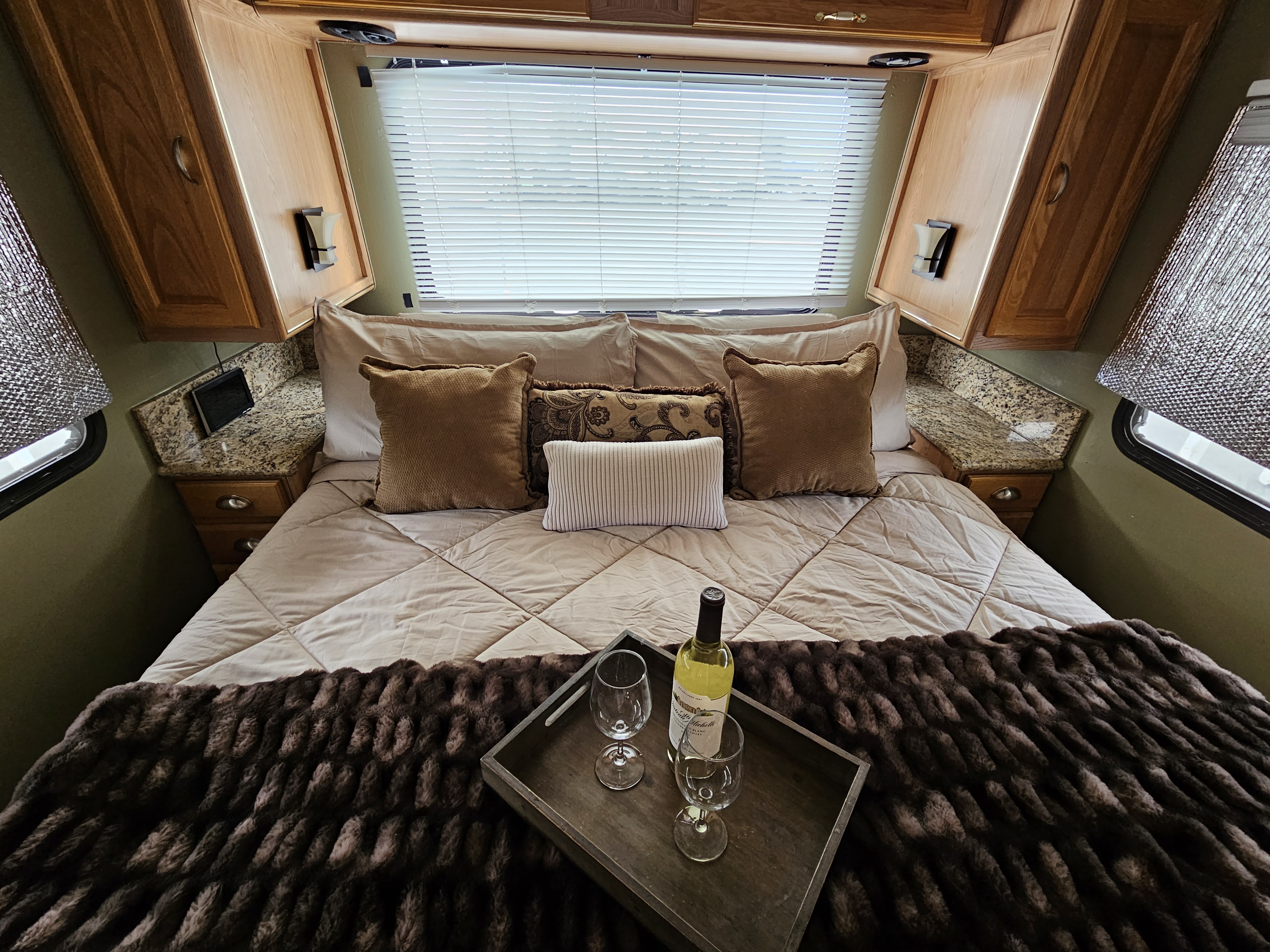 Cozy RV rental bedroom with wine & glasses on a tray, featuring wood cabinets, blinds, and a comfortable bed.. Rexhall Xl3250 1995