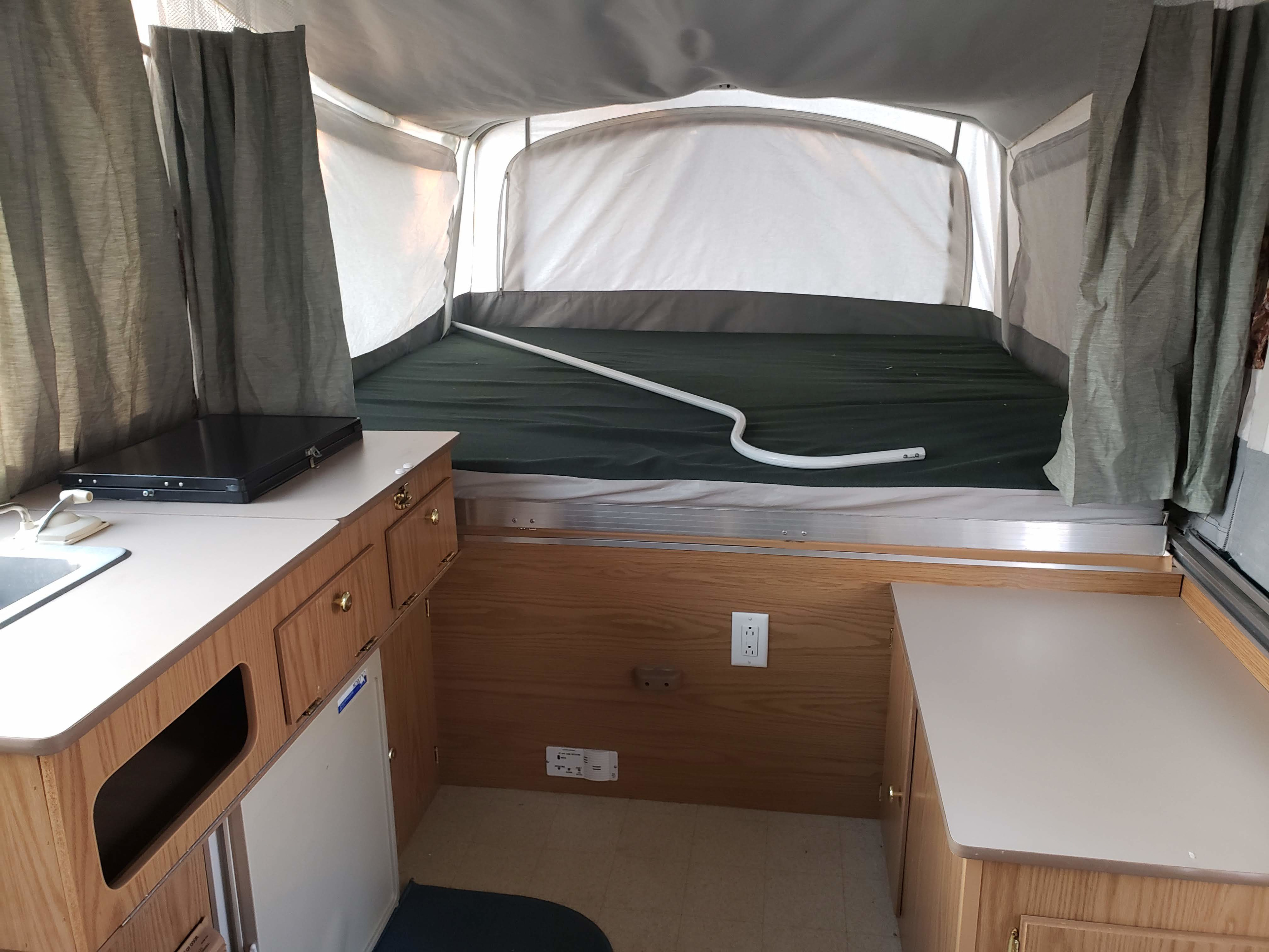 Inside this cozy RV rental: a compact kitchen with sink and stovetop, and a comfortable pop-up bunk bed.. Coleman Sedona 1999