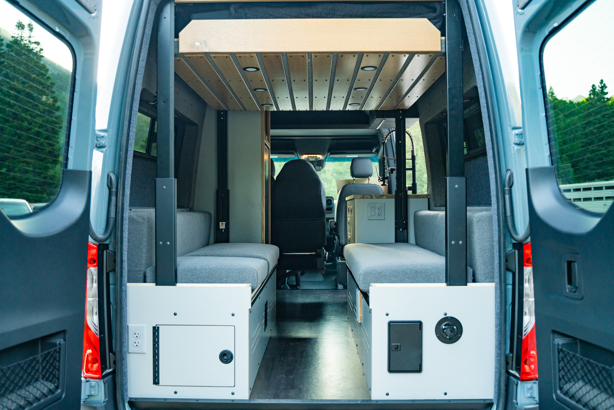 Inside a modern camper van from the rear, showing two bench beds, an overhead bed, and electricals. Ideal for rv rental.. Mercedes-Benz Sprinter 2022