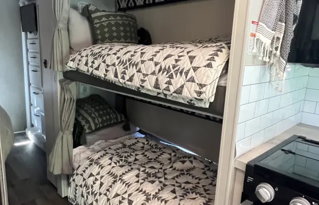 Cozy RV rental interior: view of bunk beds with patterned quilts, ample storage, and compact kitchen space.. Jayco Greyhawk 2021