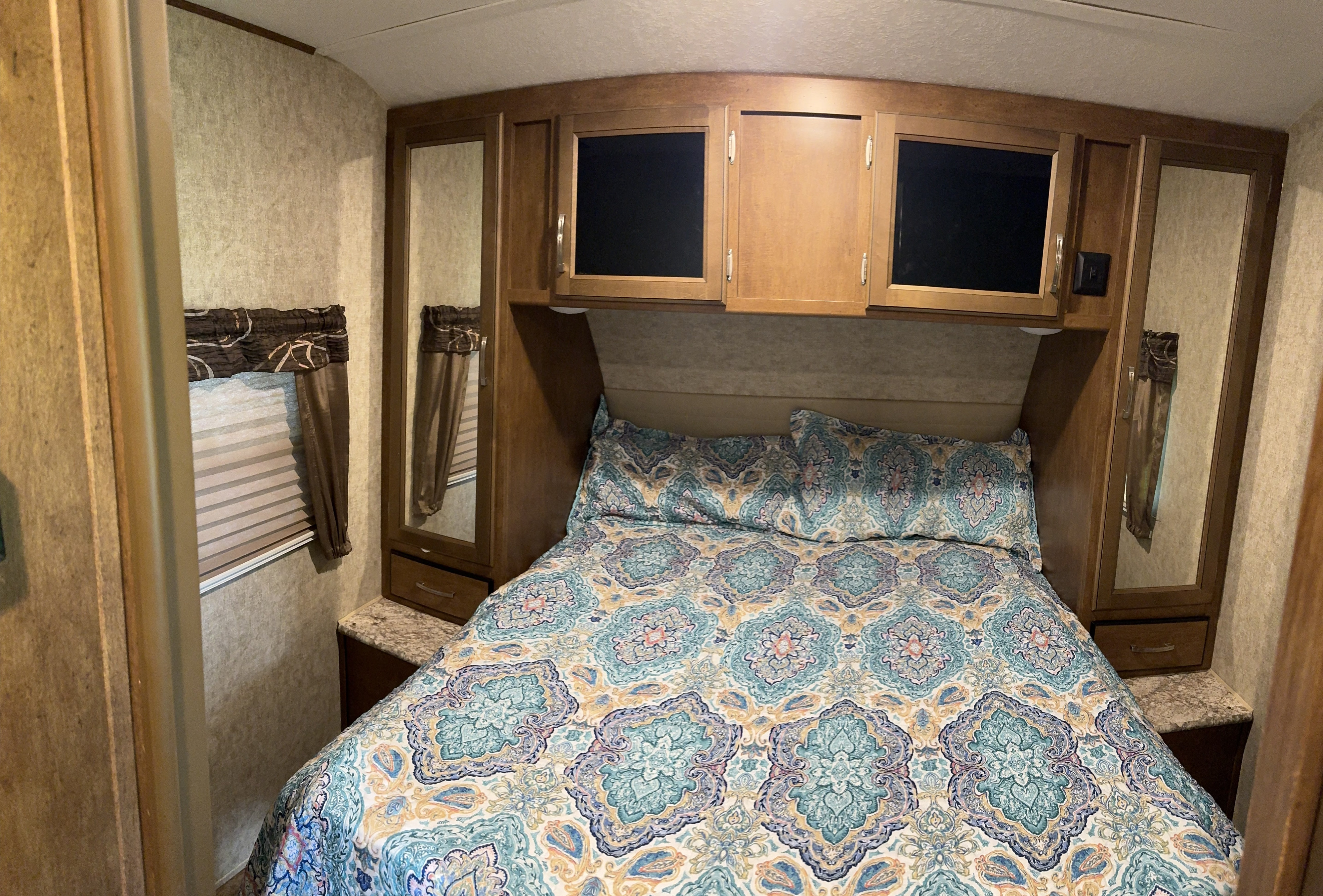 Cozy RV rental bedroom featuring a patterned bed, overhead storage, and mirrored wardrobes for a comfortable stay.. Forest River Wildcat 2017