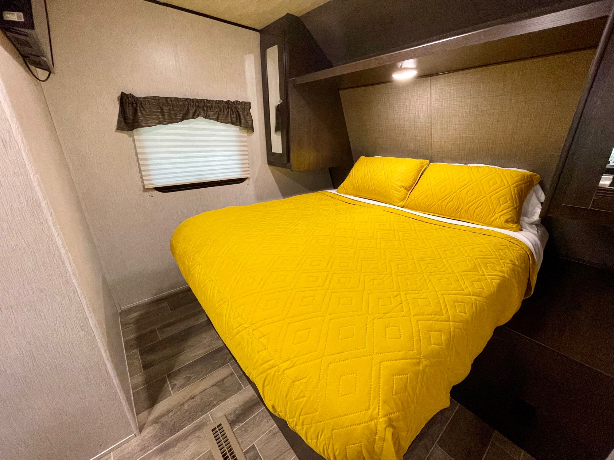 Experience comfort in this RV rental bedroom with bright yellow quilted bedding, a window, and dark wood accents.. Heartland RVs Trail Runner SLE 2019