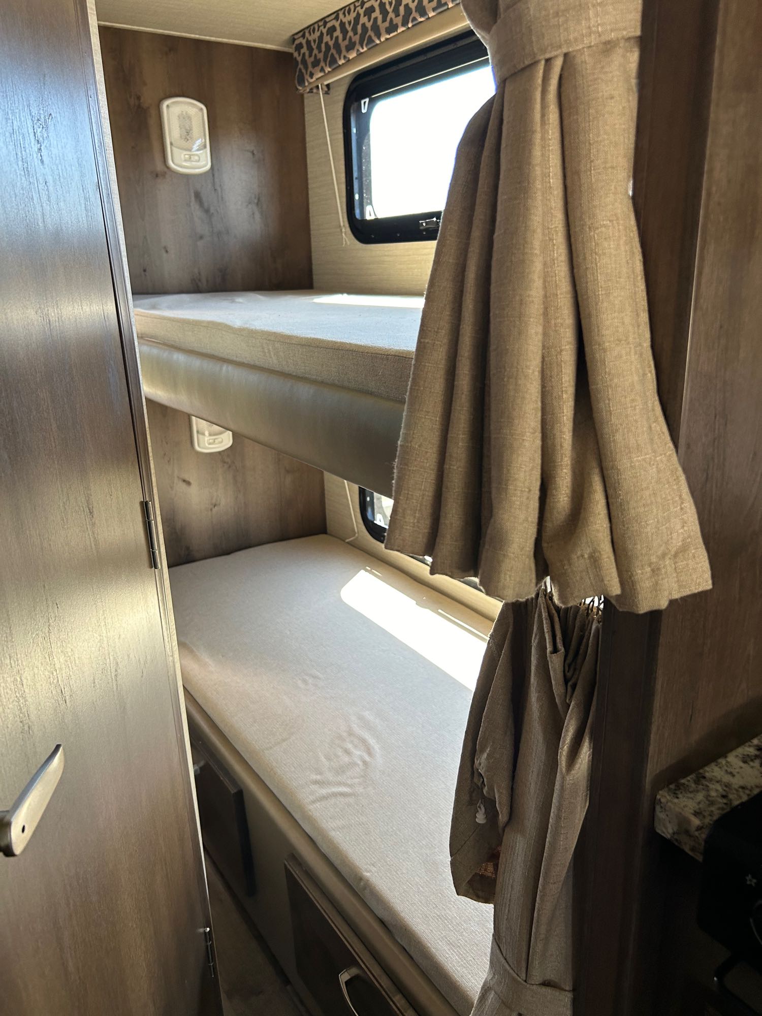 Inside an RV rental, two bunk beds with light mattresses. A window is by the lower bunk, and a reading light is on the wall.. Redhawk 31F MC 2019