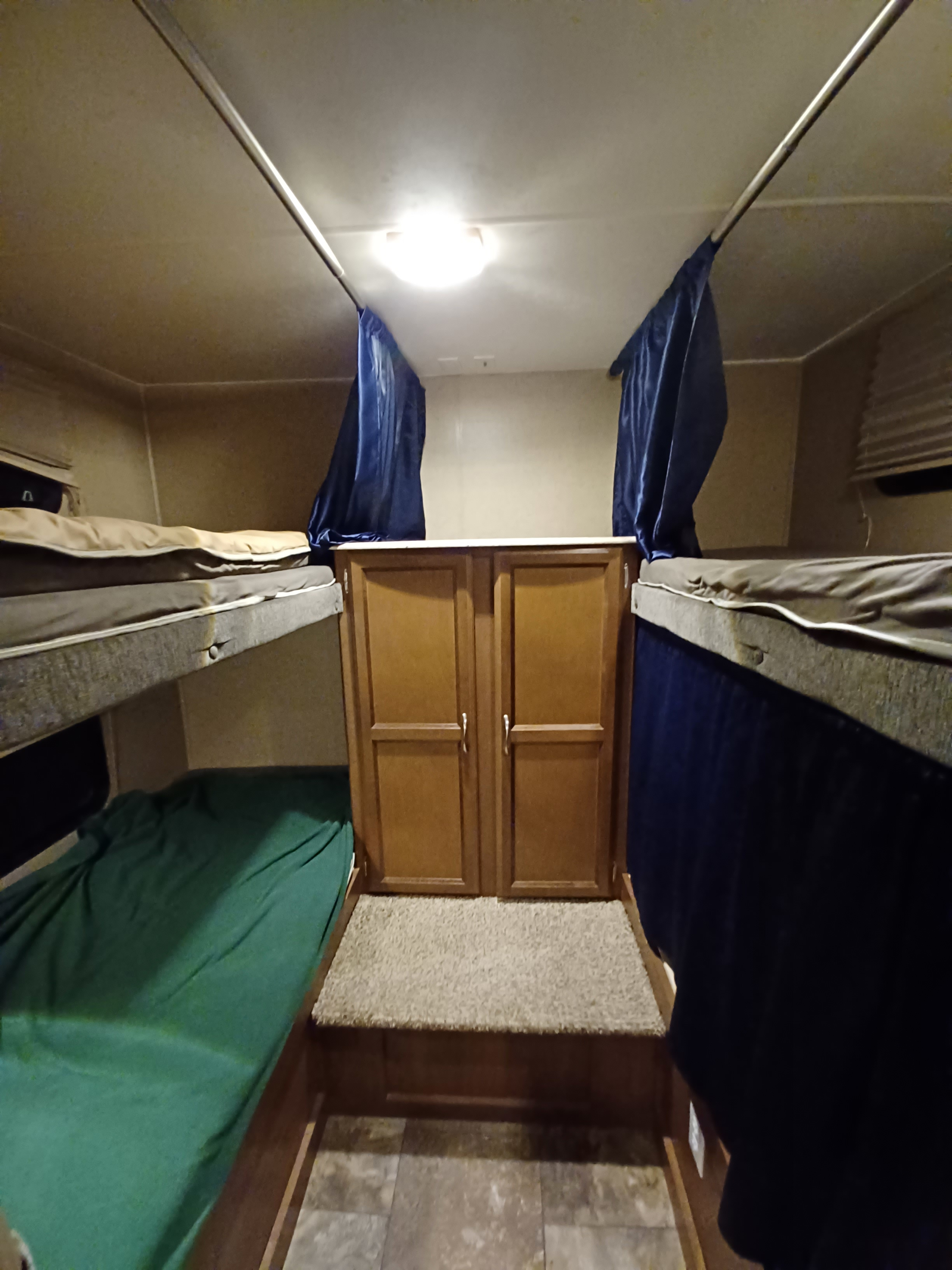 RV rental interior shows two sets of bunk beds with blue privacy curtains, flanking wood cabinets over carpet & tile.. Coachmen Freedom Express Liberty Edition 2016