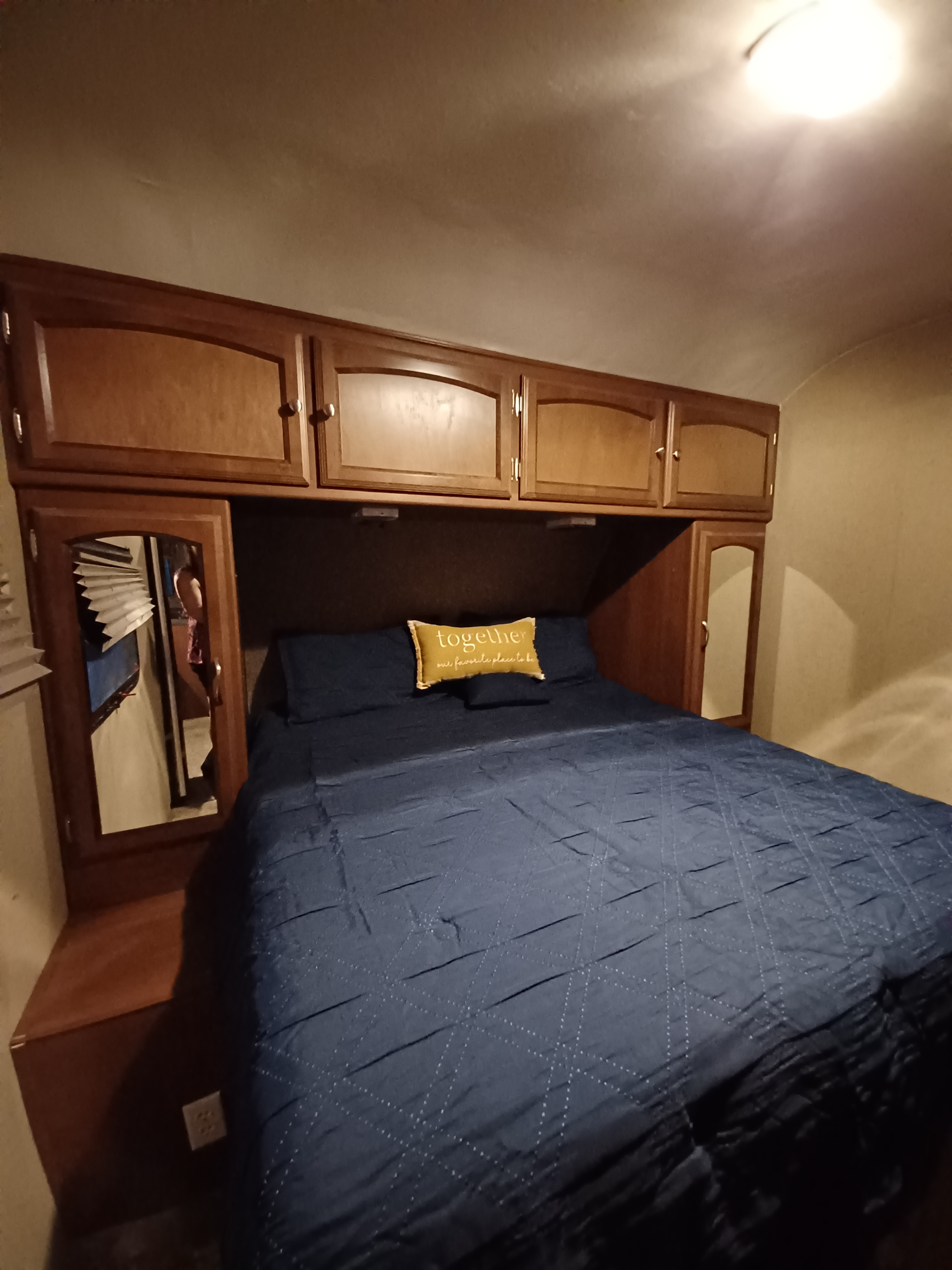 RV rental bedroom with a blue quilted bed, yellow "together" pillow, and built-in wooden cabinetry.. Coachmen Freedom Express Liberty Edition 2016