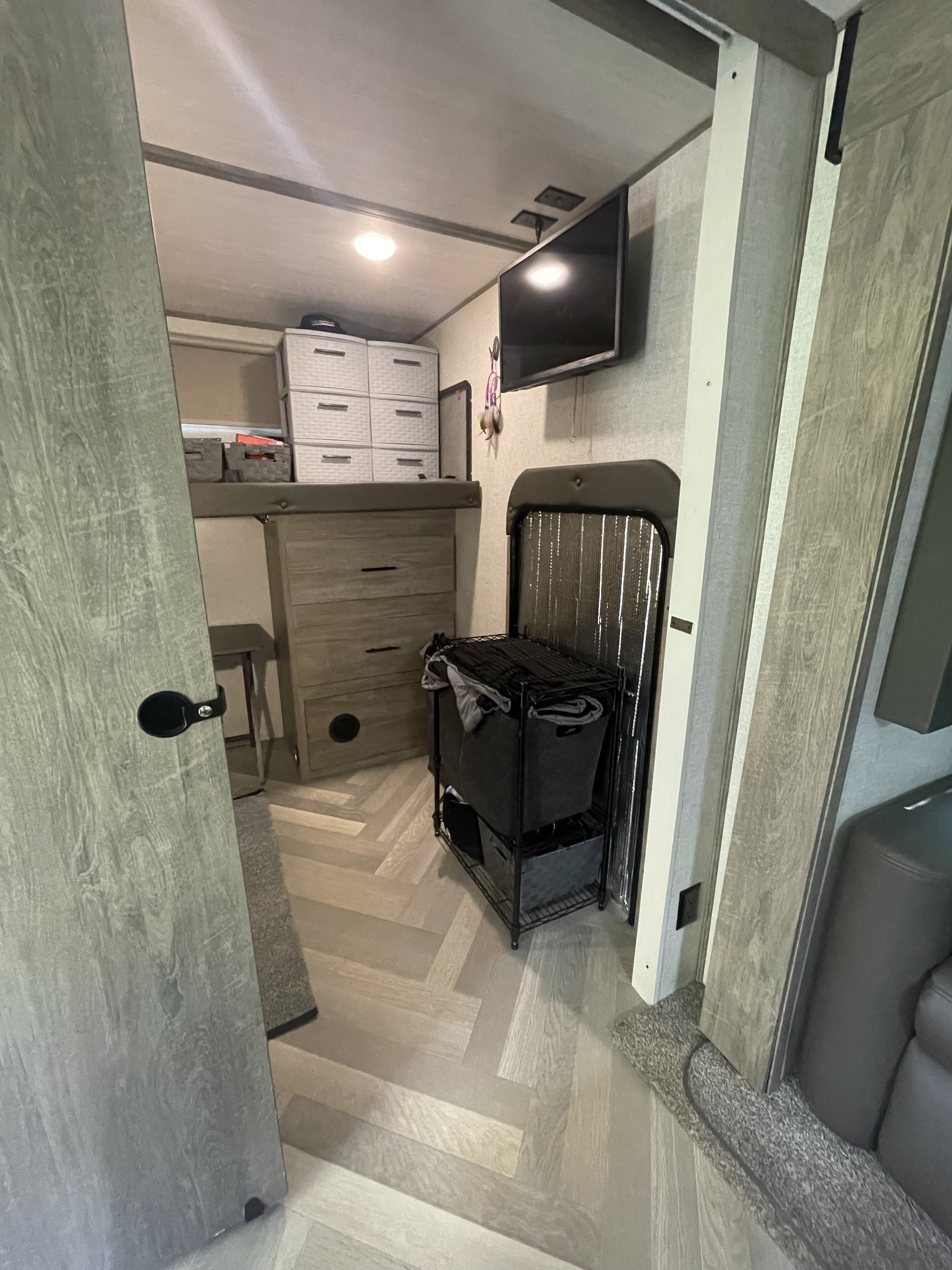 Inside an RV rental: a compact bedroom featuring a bunk bed, dresser storage, wall-mounted TV, and laundry area.. Forest River Wildwood Heritage Glen HL 2021