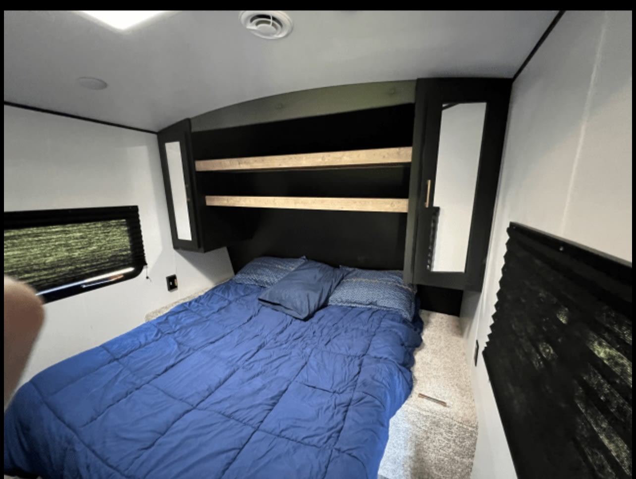 Relax in this cozy RV rental bedroom featuring a comfortable blue bed, overhead storage, and windows with blinds.. Keystone RV Springdale 2022
