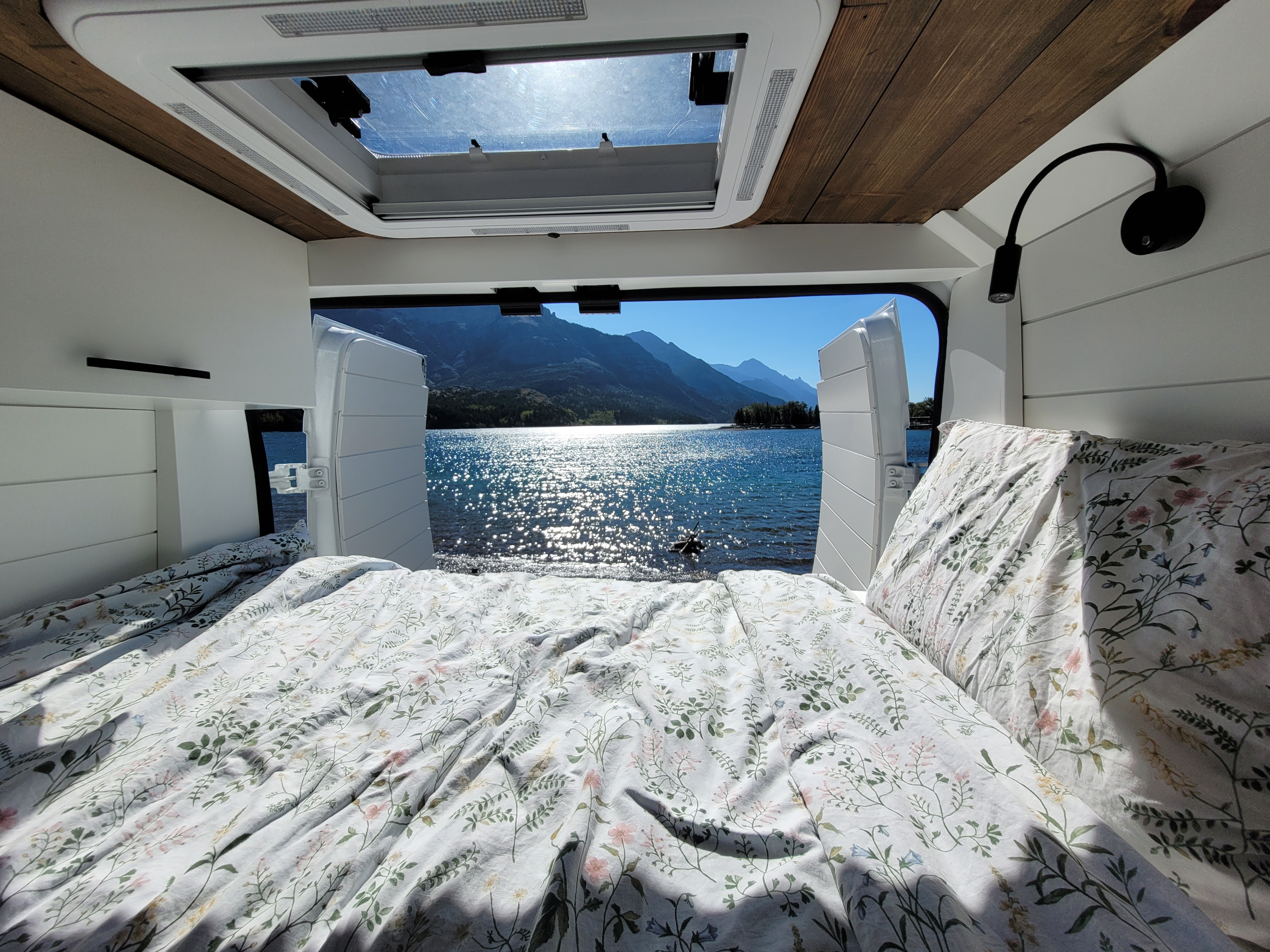 Waking up to stunning lake & mountain views from a floral-patterned rv rental bed. Ideal for camper van travel.. Ram Promaster 3500 159 Ext 2022