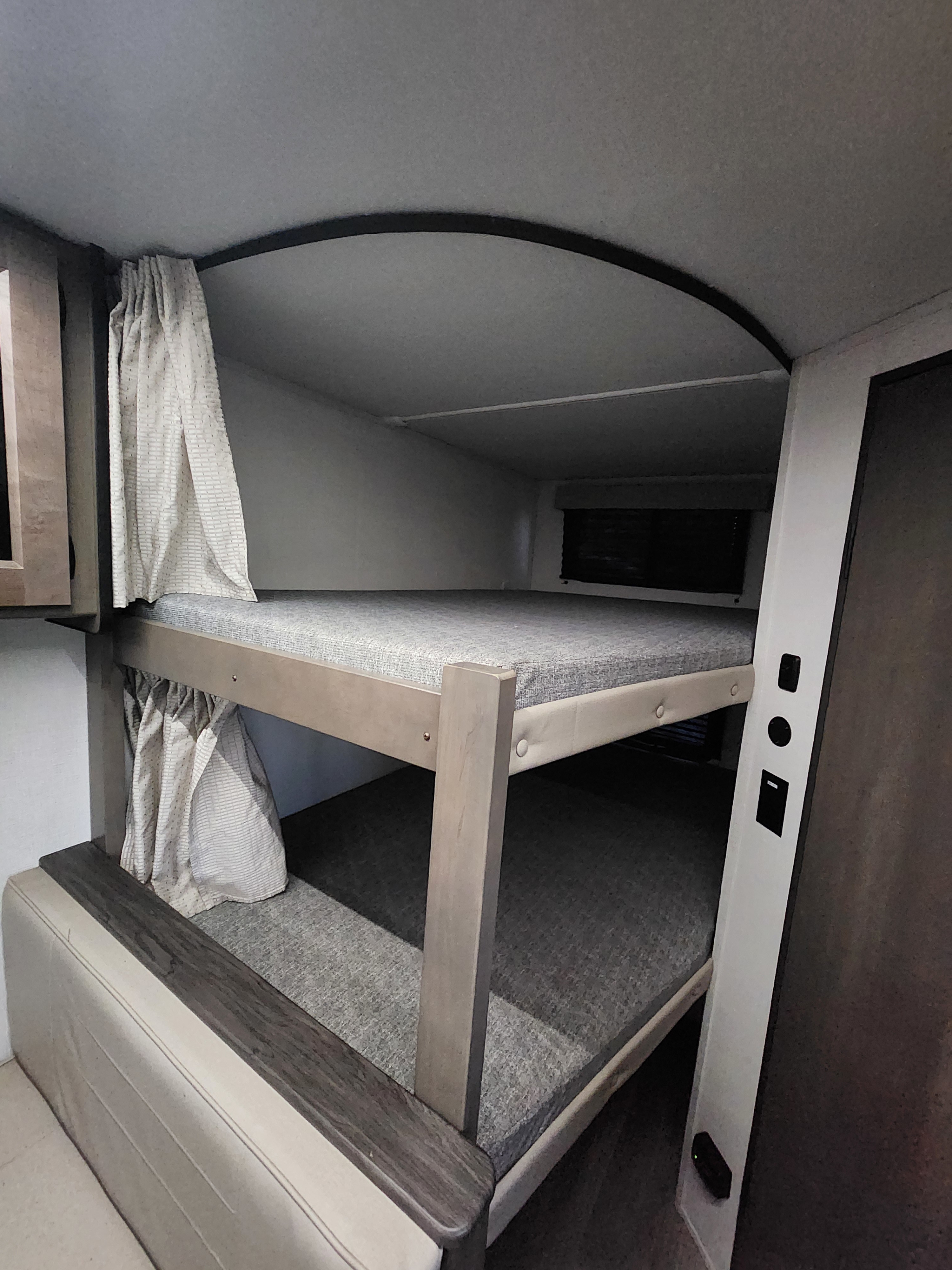 Functional bunk beds in an RV rental, featuring grey mattresses, light wood frames, and privacy curtains for cozy sleeping.. Grand Design Transcend Xplor 2024