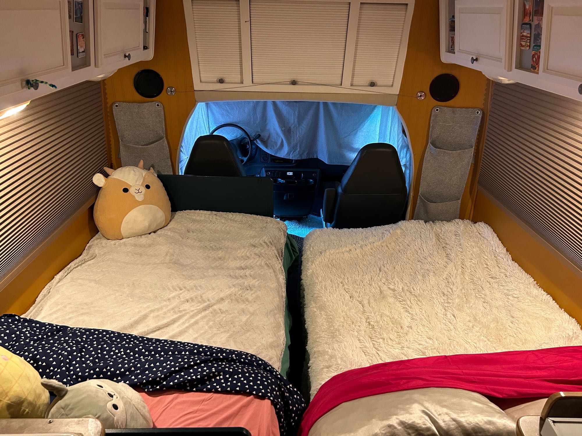Inside a comfy RV rental: two beds with blankets & plushies, facing the front seats and a blue privacy screen.. R-Vision Trail-Lite B+ 2003