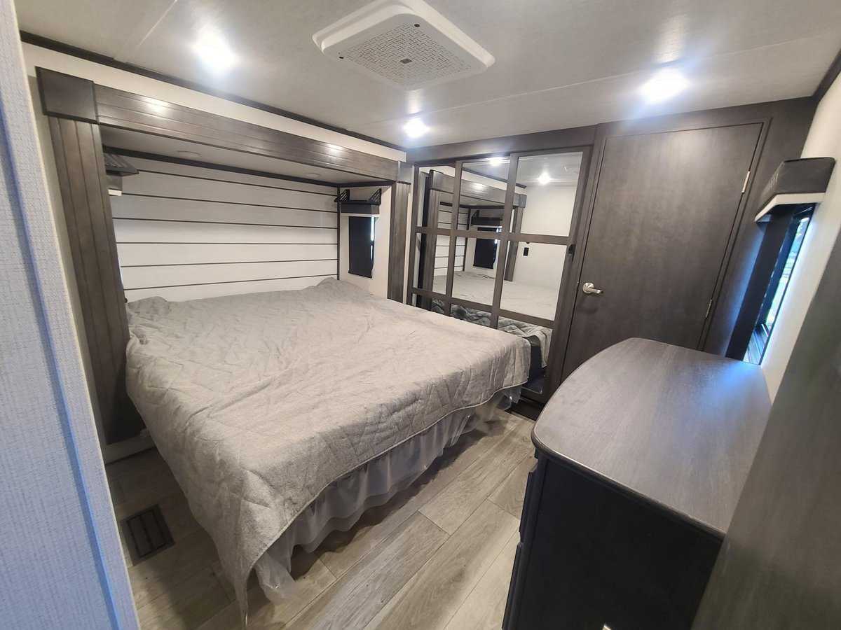Explore this modern RV rental bedroom featuring a full bed, shiplap wall, wood floors & built-in storage for your travels.. Keystone RV Cougar 2024