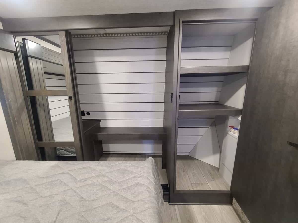 RV rental bedroom: ample storage with mirrored closet, shelves, a bench, and a compact washer/dryer unit.. Keystone RV Cougar 2024